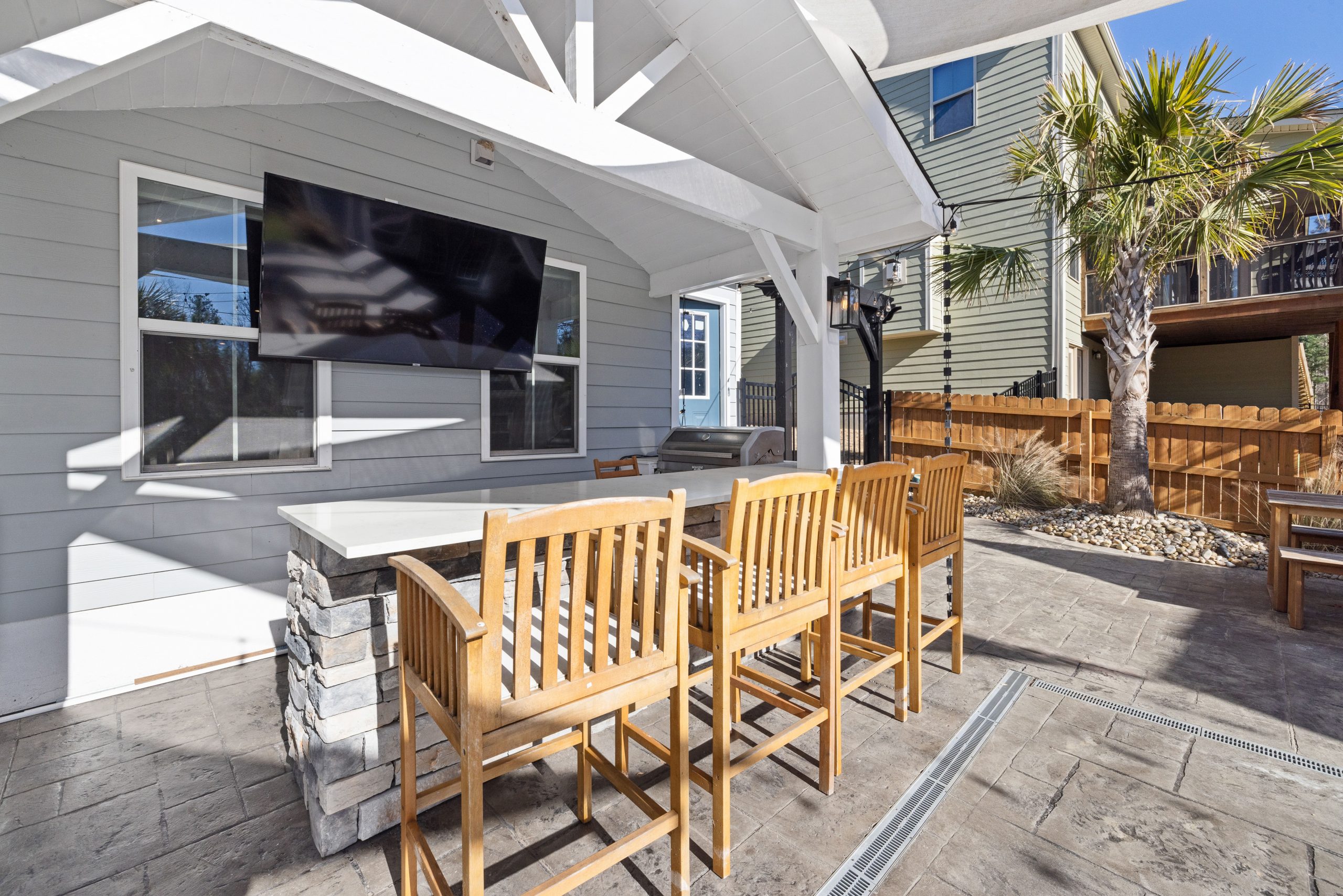 Spacious patio featuring wooden seating, stone bar, and wall-mounted TV under a covered area.