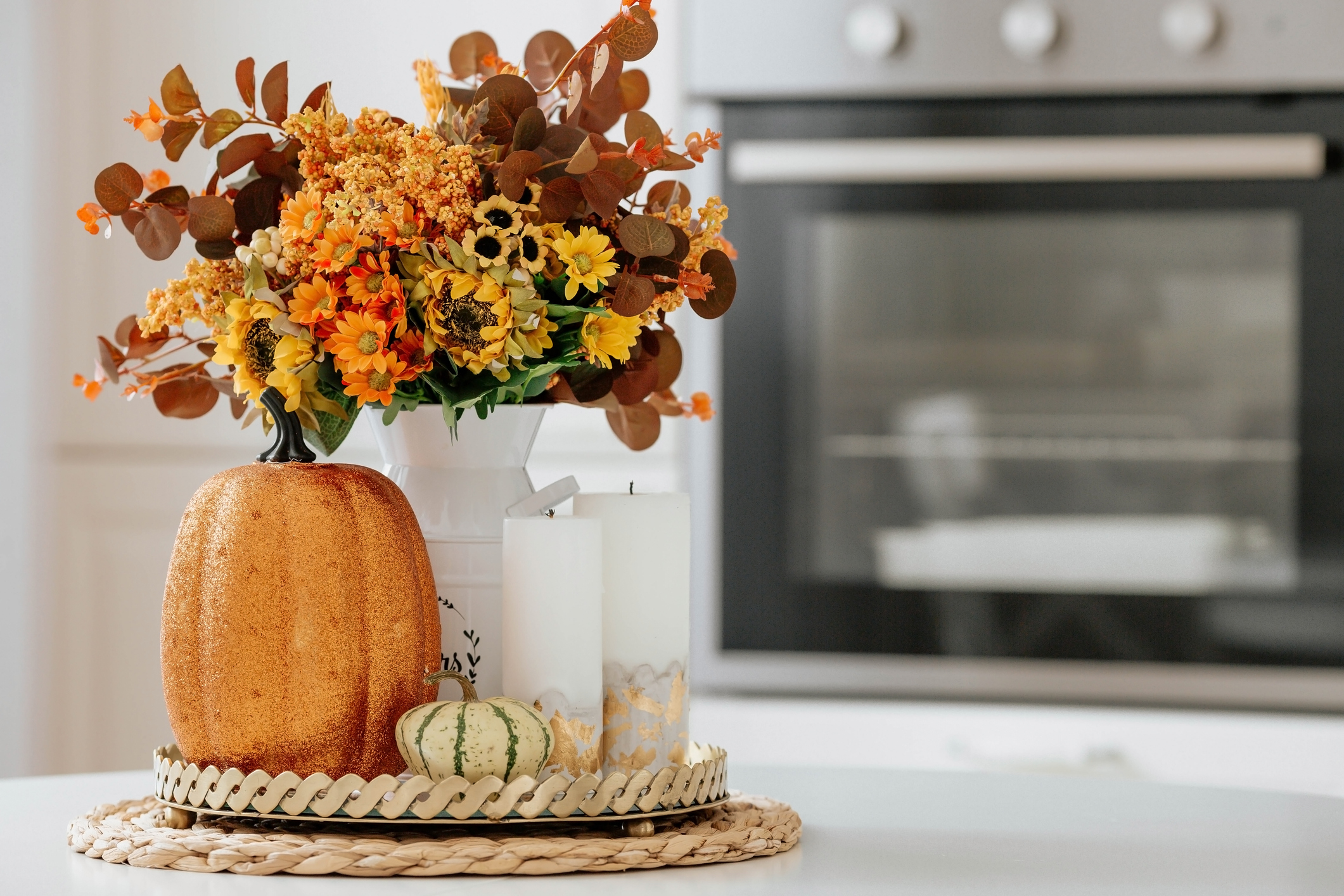 Still-life. Yellow, orange flowers in a vase, pumpkins and candles on a golden tray on a white table in a home kitchen interior. A cozy autumn concept. | Blain's Farm & Fleet