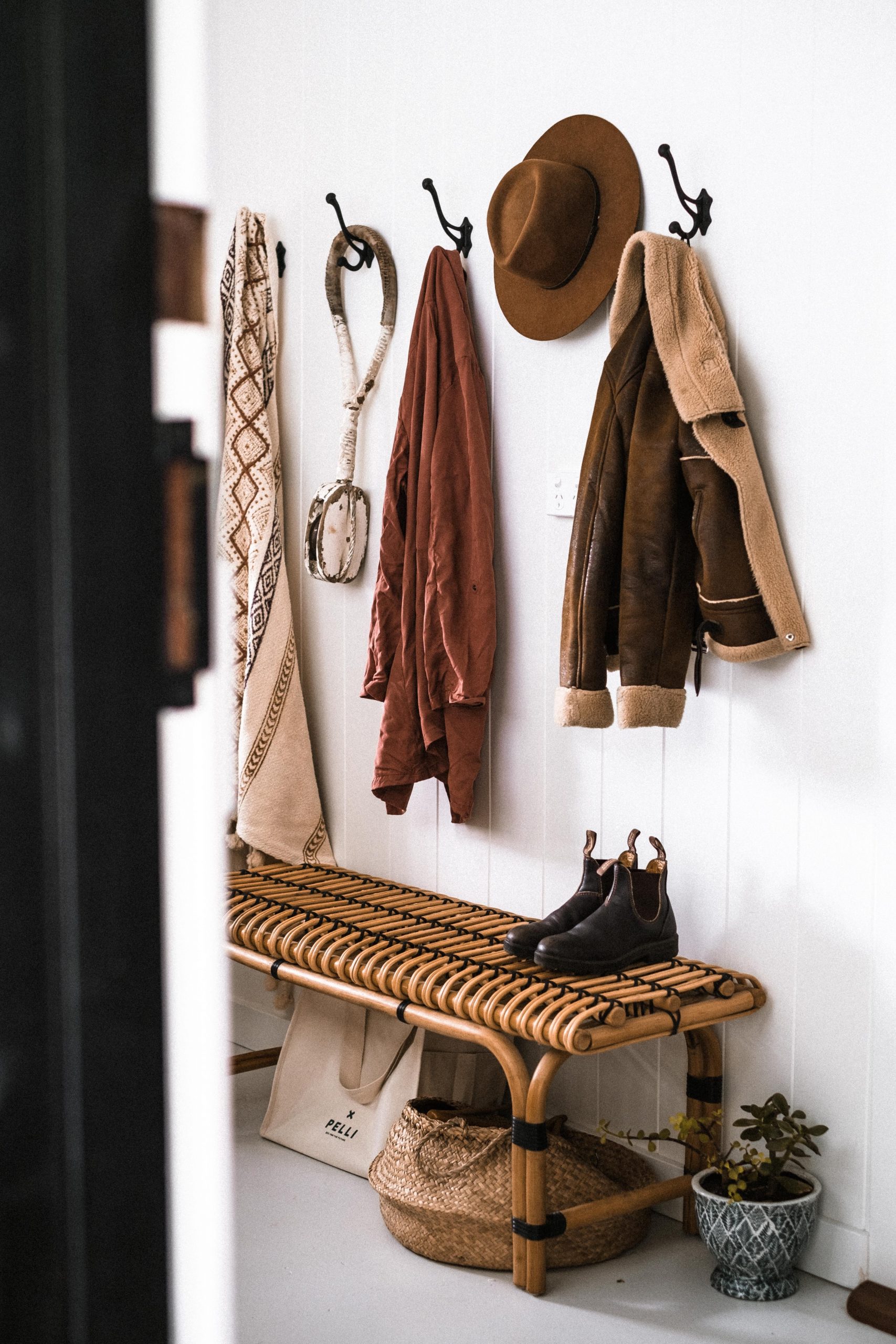 Stylish entryway decor with coats, hat, and boots on rattan bench.