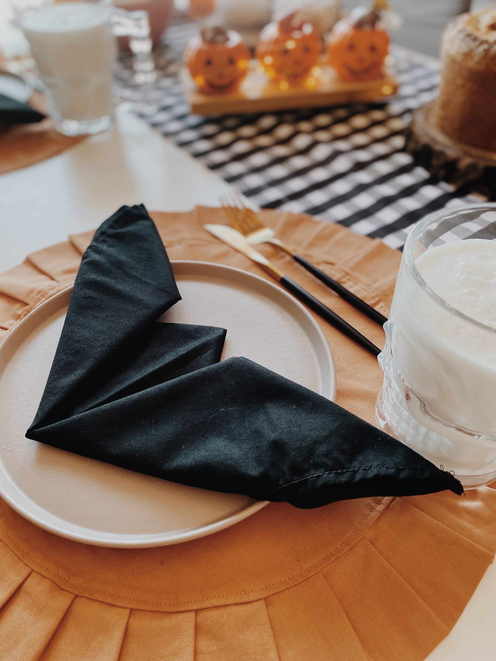 Stylish Halloween table setup with black napkins and pumpkin decor in São Paulo.
