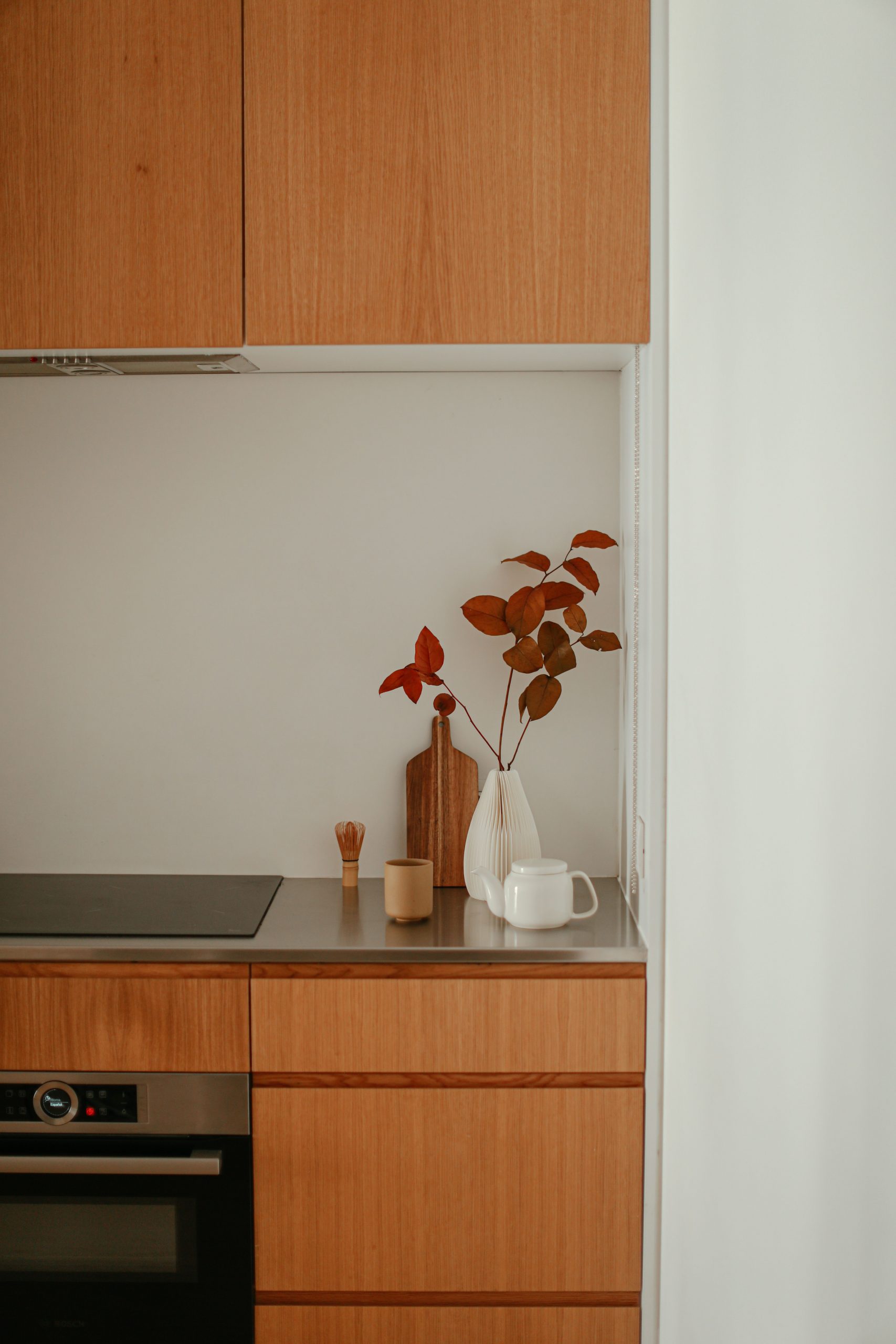 Stylish modern kitchen featuring minimalist design with autumn floral decor and sleek wooden cabinets.