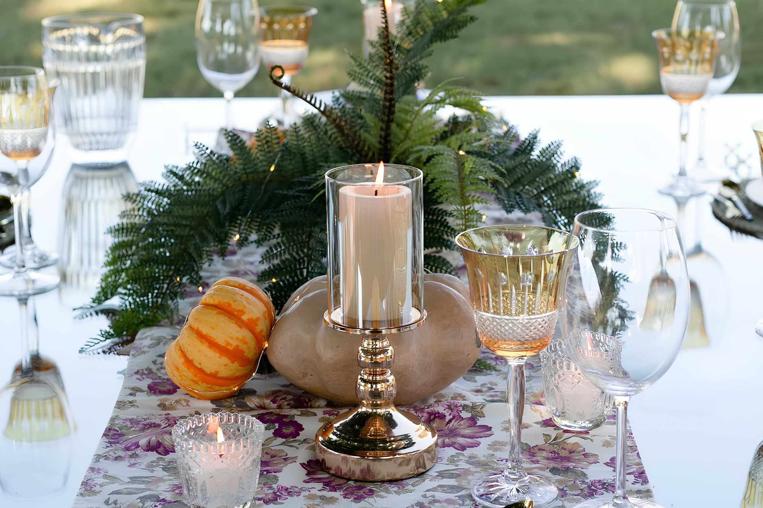 Stylish outdoor table arrangement with candle, glassware, and foliage centerpiece.
