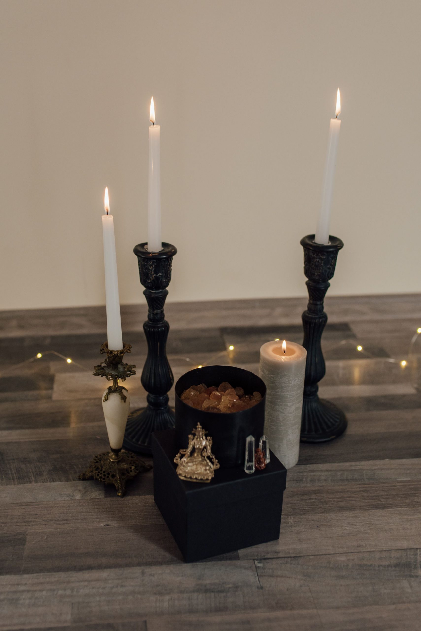 Three tall candlesticks and a pillar candle create a warm, serene atmosphere on a wooden floor.