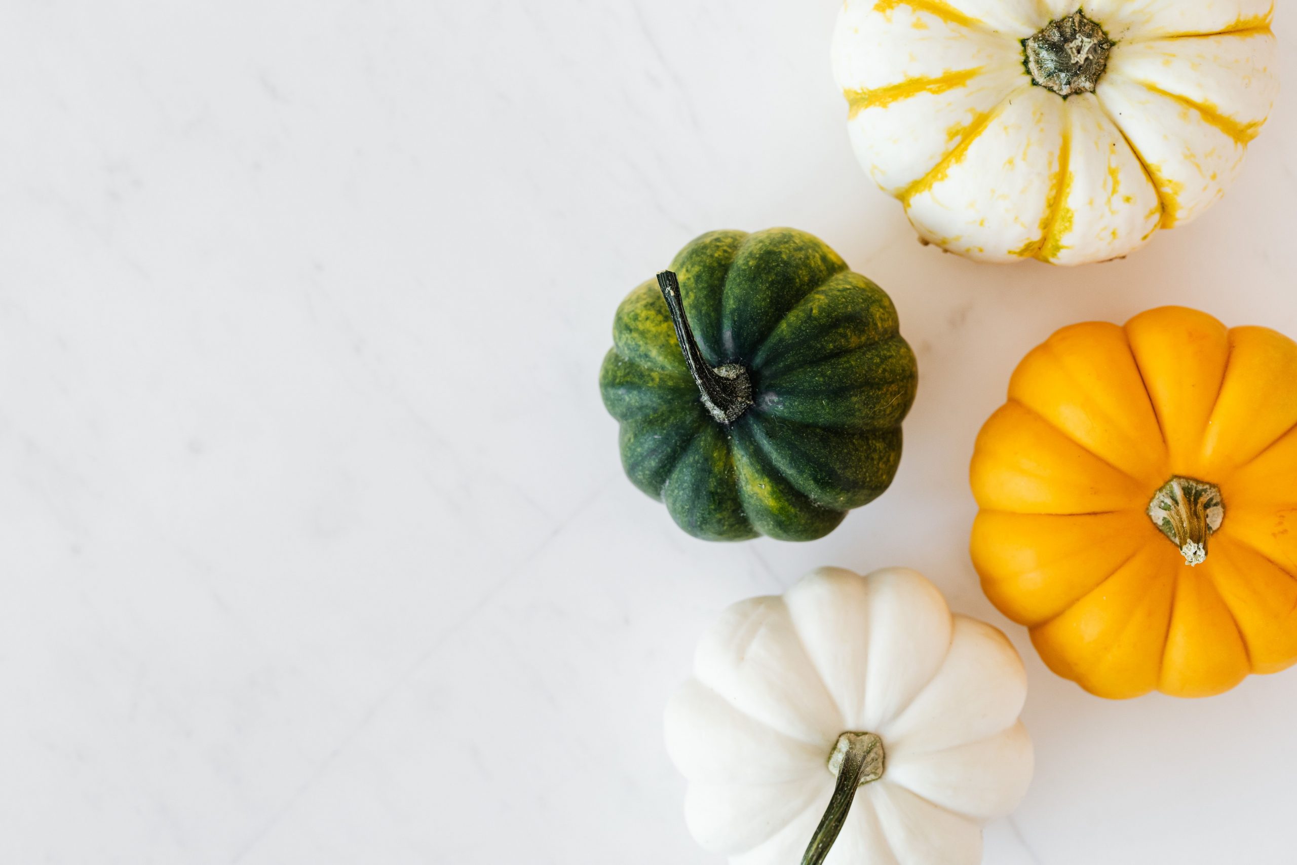 Top view of colorful mini pumpkins on a white marble background, perfect for autumn themes.