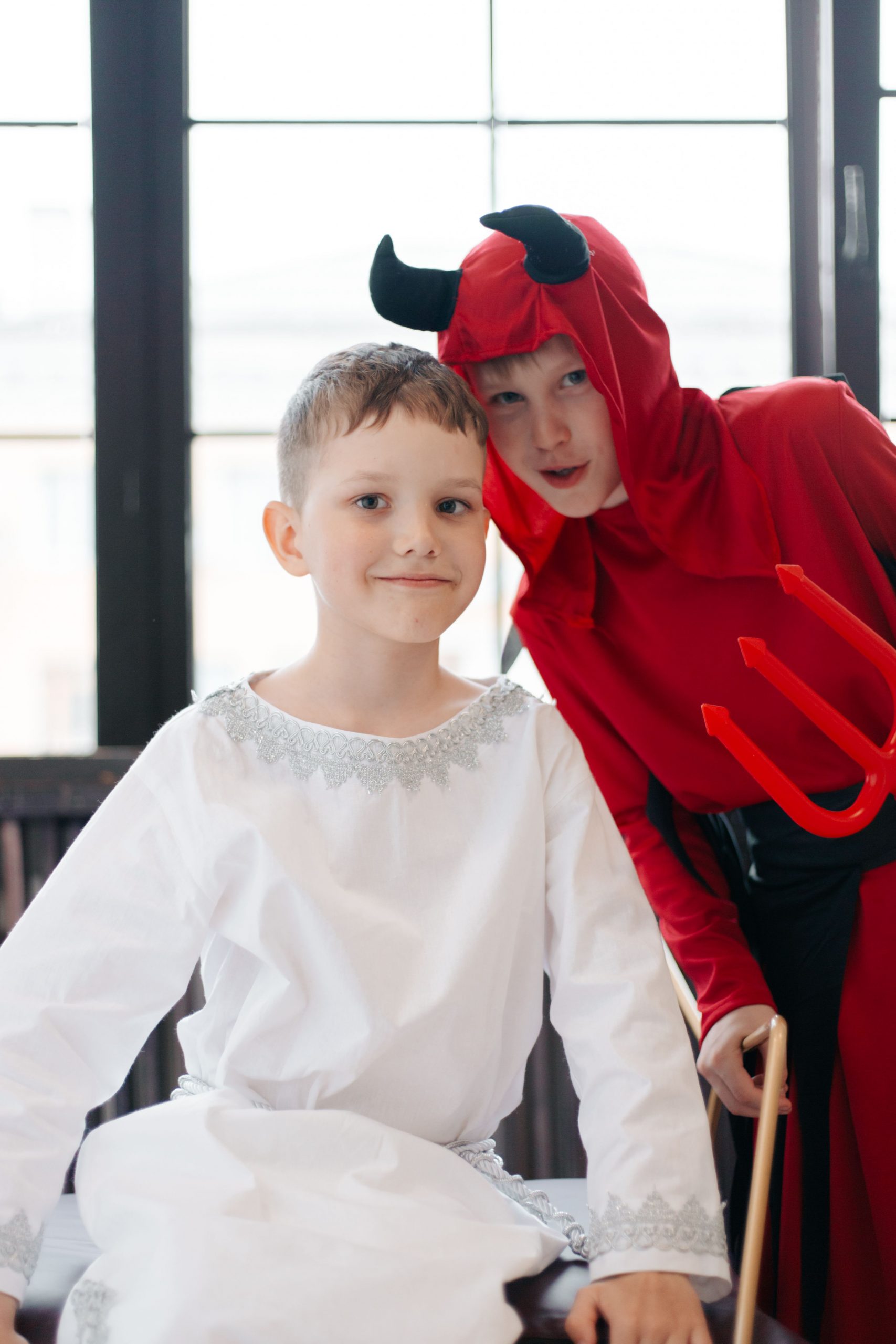 Two boys dressed as an angel and a devil posing for Halloween indoors.
