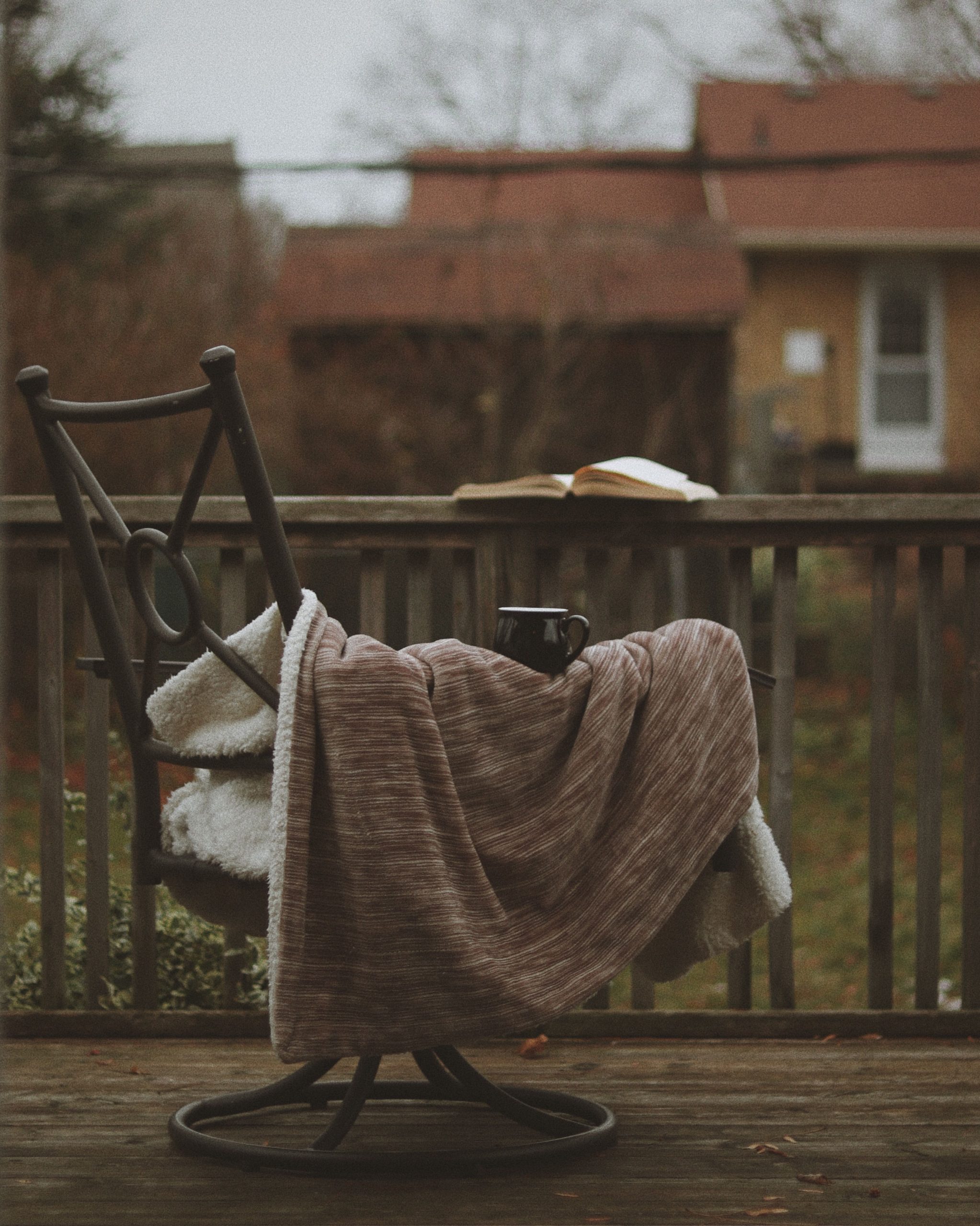 Warm and inviting autumn porch scene with a blanket-covered chair, a book, and a mug.
