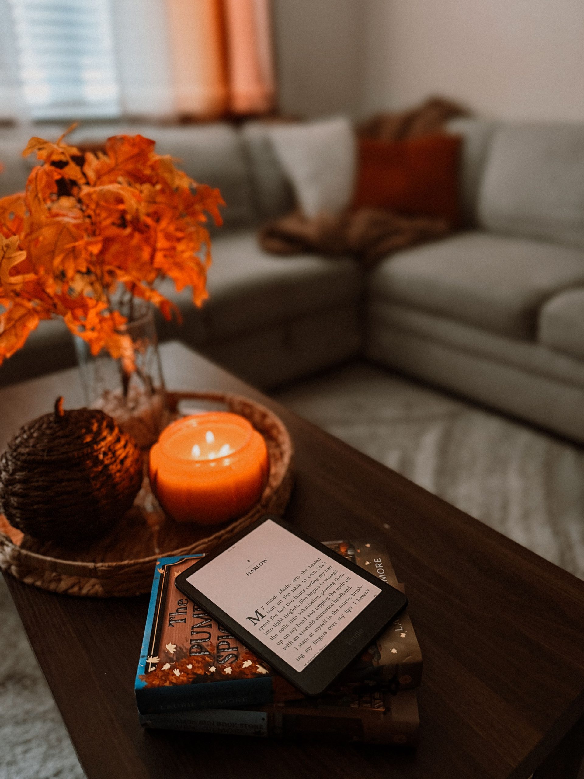 Warm and inviting living room with fall decorations, candlelight, and an e-reader on a coffee table.
