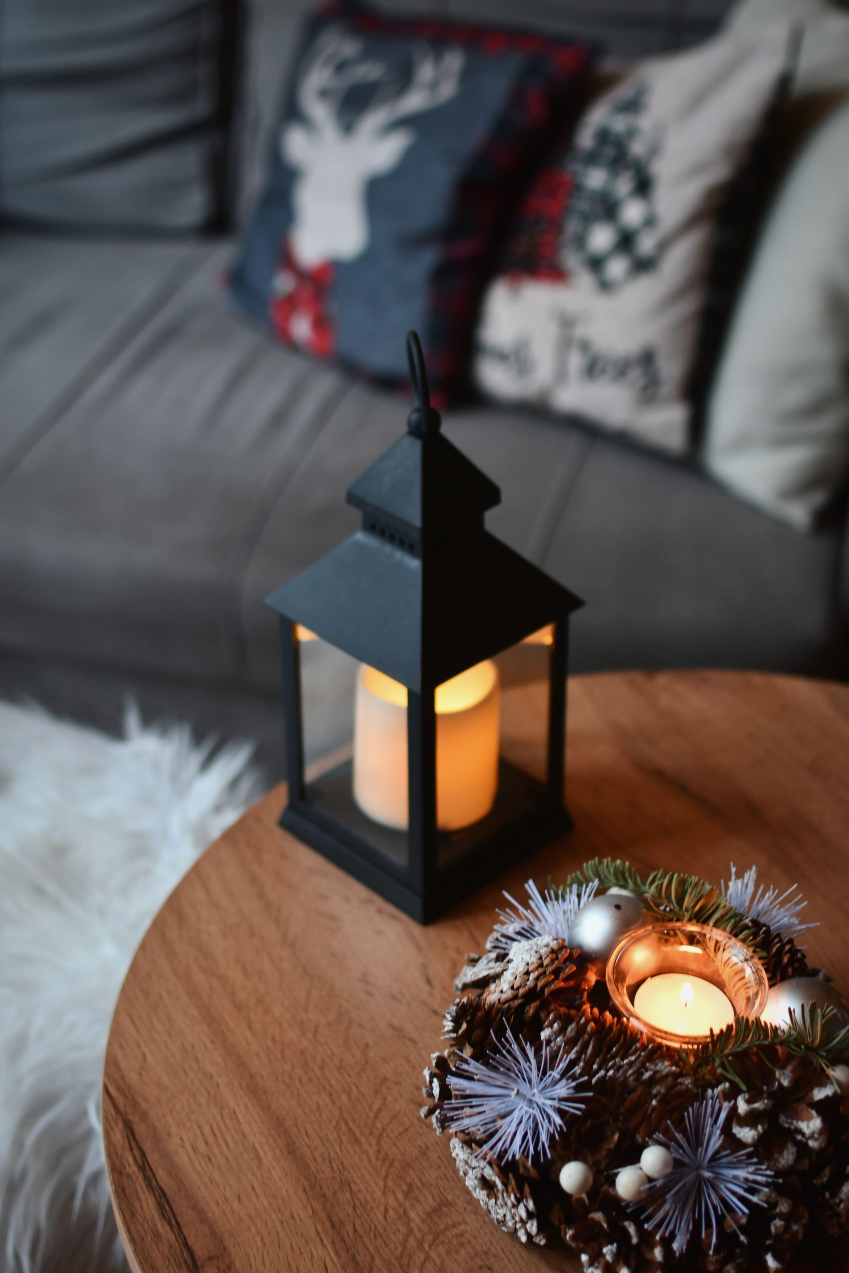 Warm and inviting winter home decor featuring a candle lantern on a wooden table with a holiday wreath.