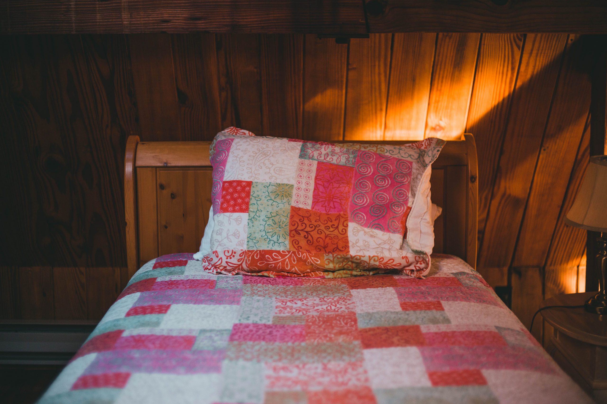 Warm and inviting wooden cabin bedroom featuring a colorful patchwork quilt and pillow.