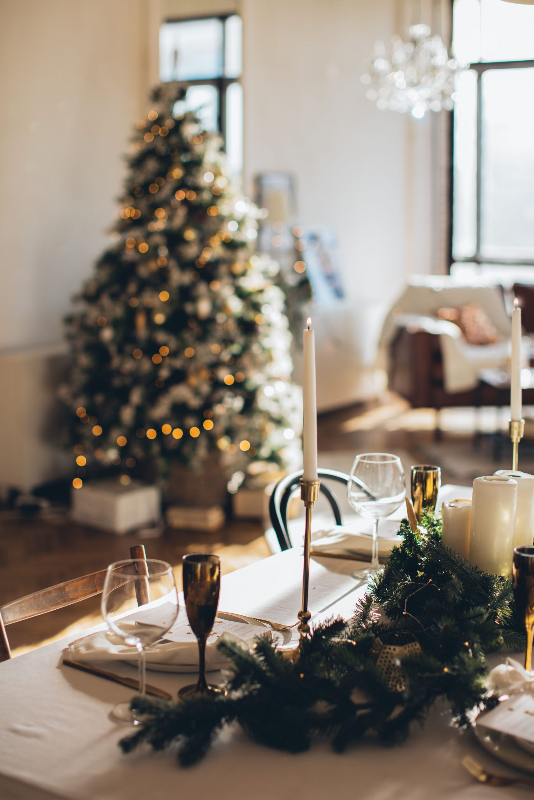 Warm and luxurious Christmas table setting with candles and a decorated tree in the background.