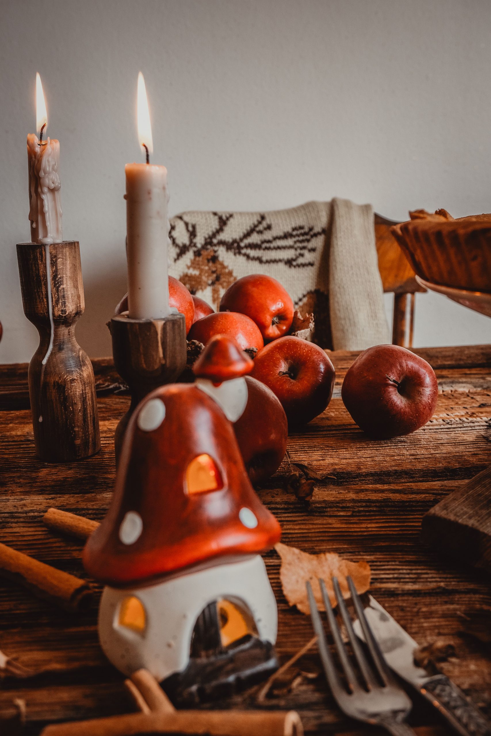 Warm autumn decor with apples, candles, and a mushroom ornament on a rustic wooden table.