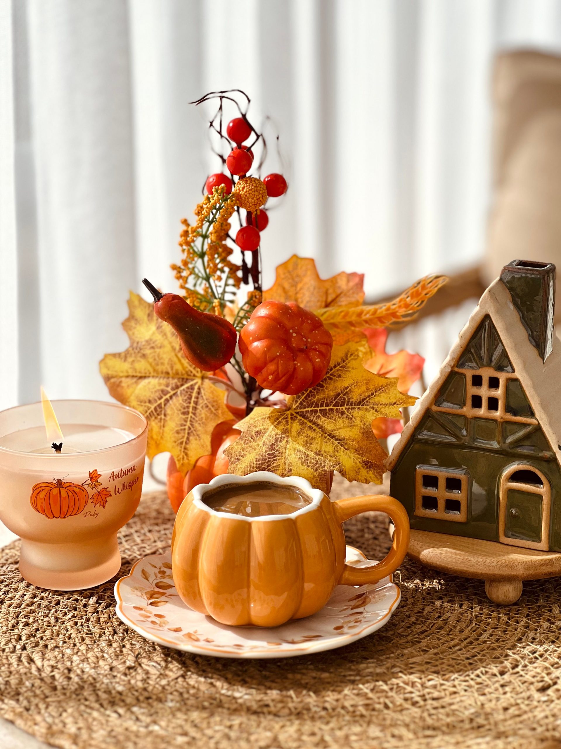 Warm autumn scene featuring pumpkin decor and candle on woven mat.