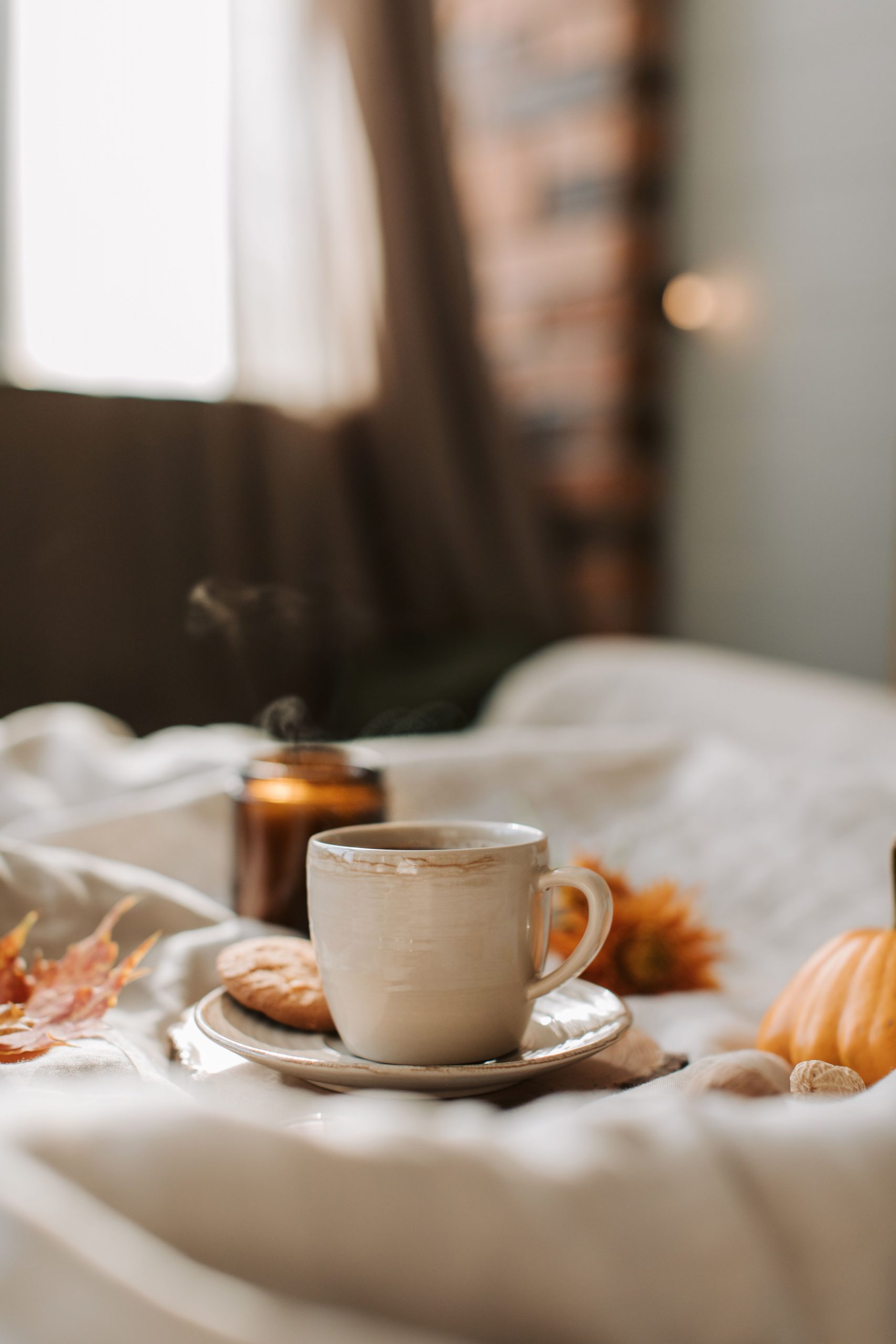 Warm autumn scene with a steaming cup of coffee, cookies, and seasonal decor on a bed.