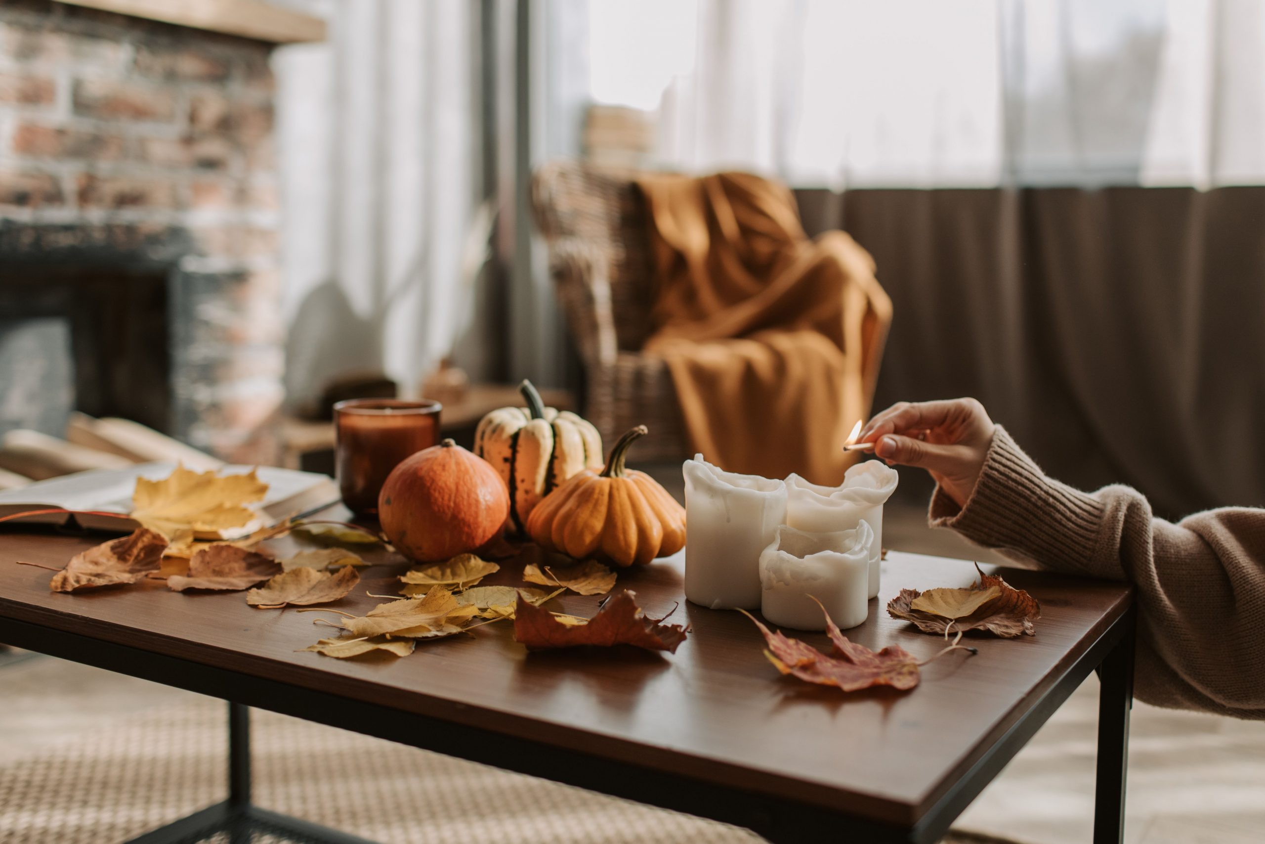 Warm autumn scene with candles, pumpkins, and leaves on a wooden table indoors.