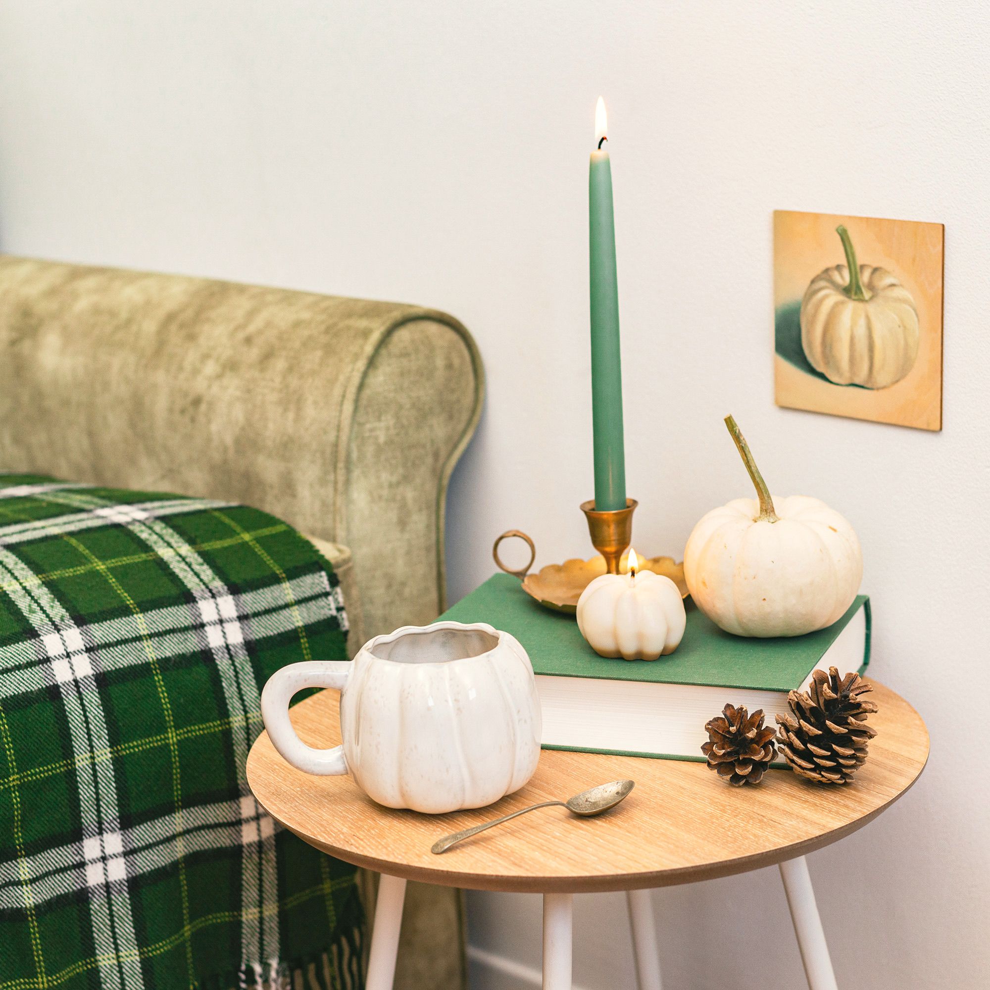 Warm autumn scene with candles, pumpkins, and pine cones on a coffee table.