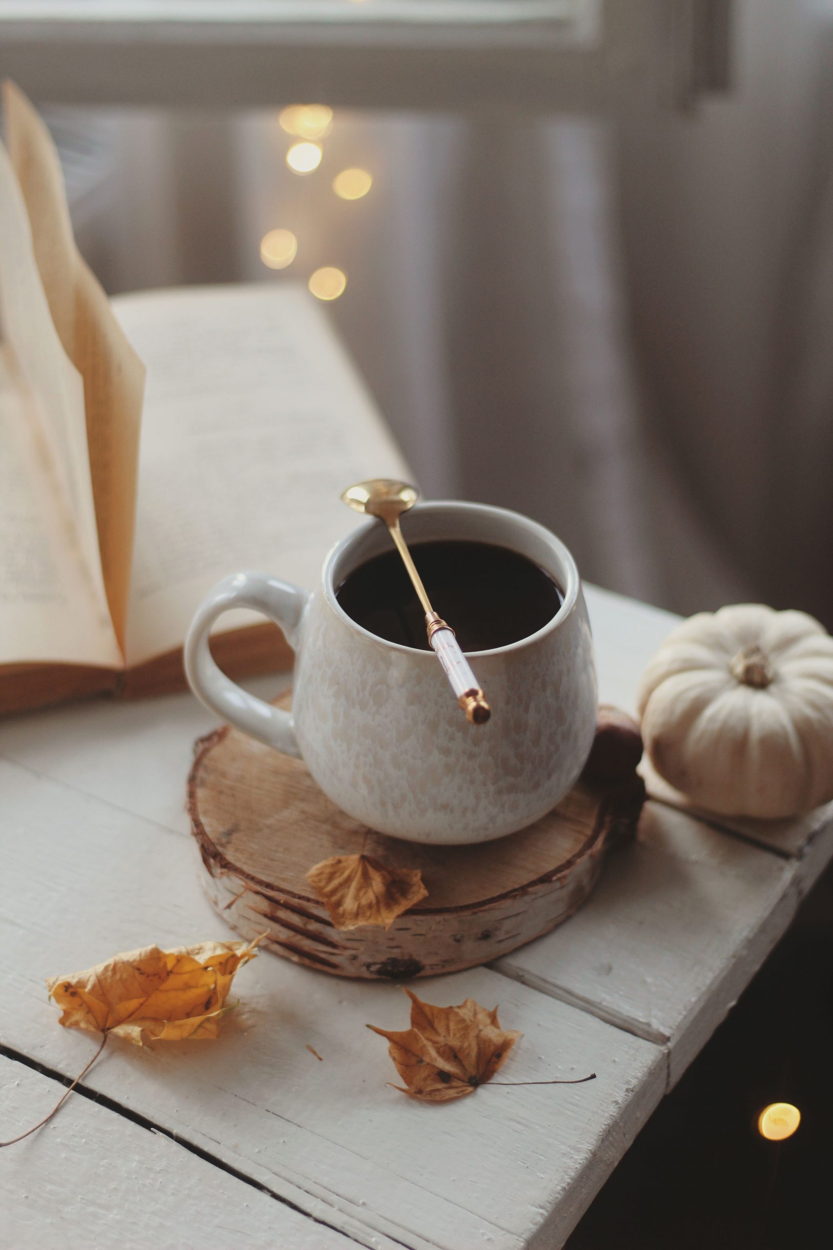 Warm autumn setting with coffee, pumpkin, and book on a rustic table indoors.