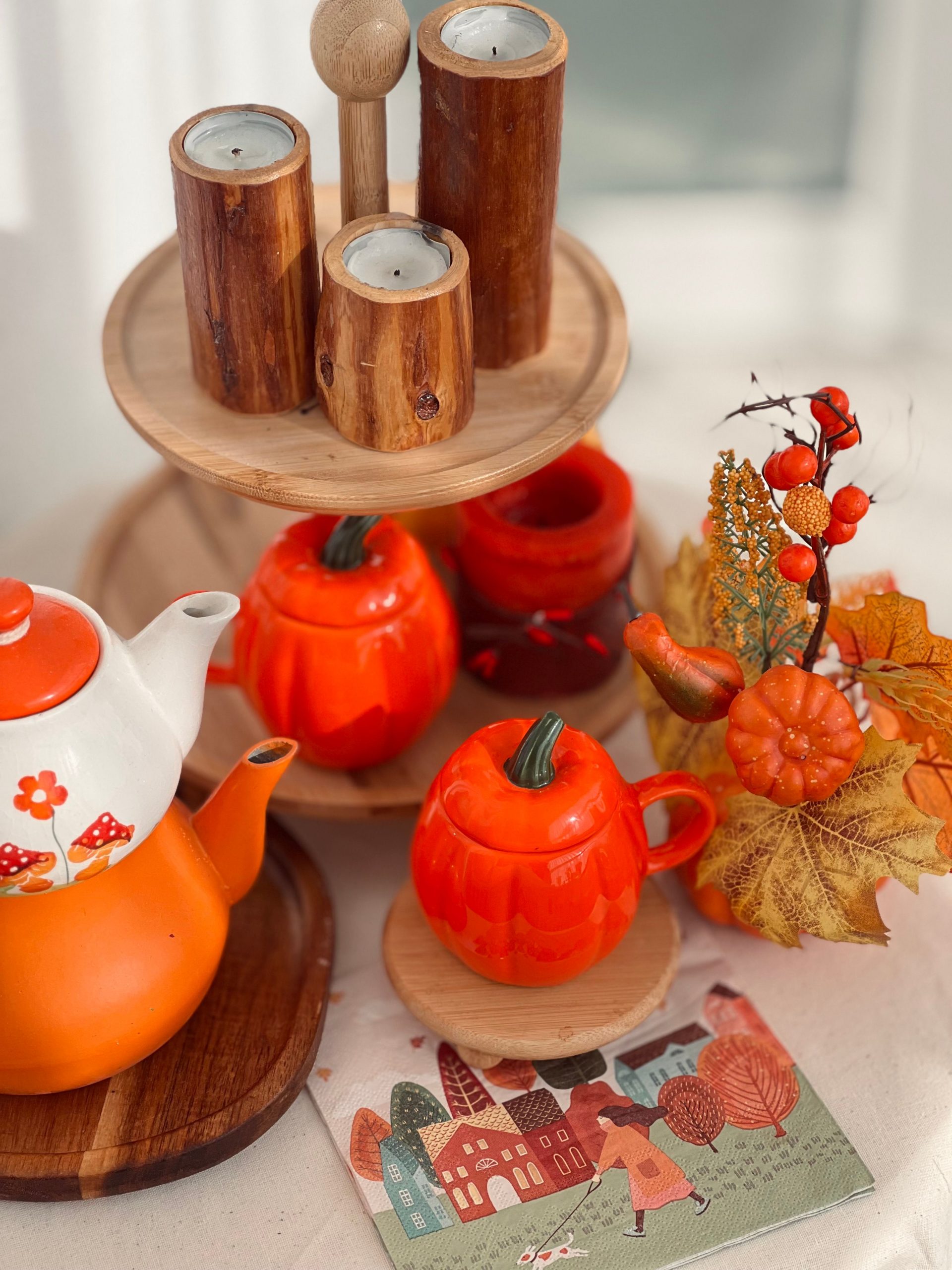 Warm autumn-themed display with orange teapot and pumpkin decorations on wooden trays.