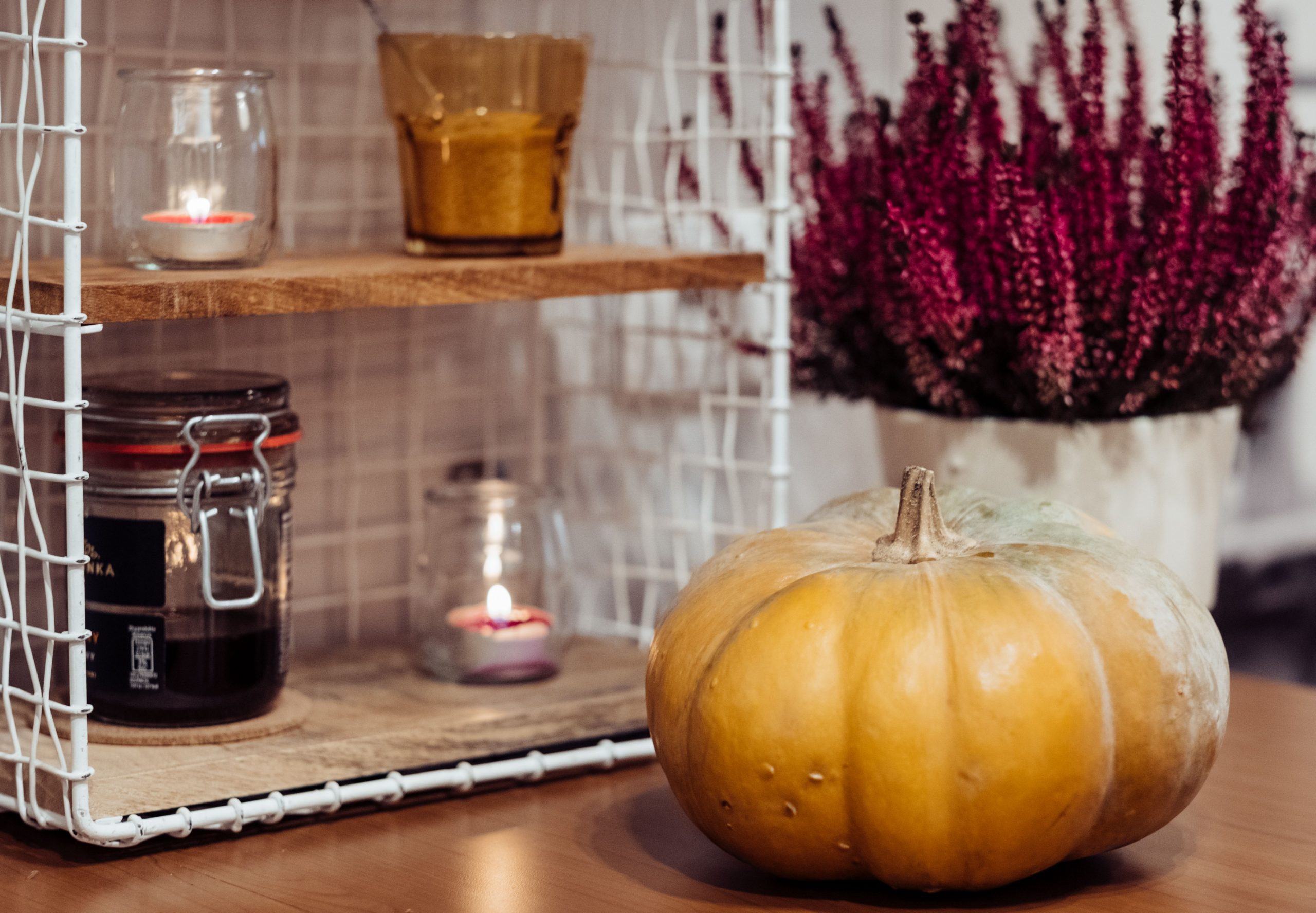 Warm, autumnal indoor setting with candles, pumpkin, and heather plant.