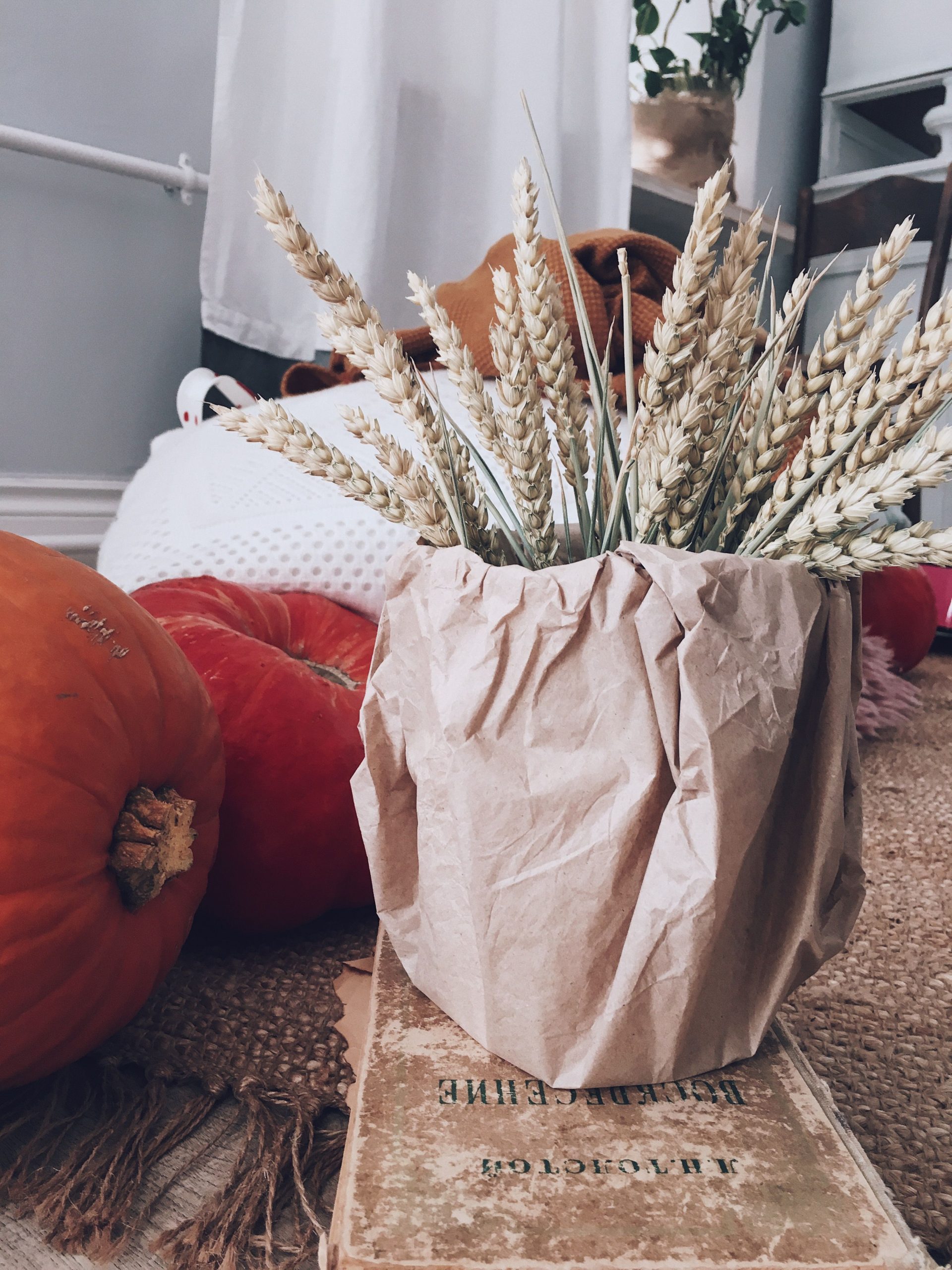 Warm fall arrangement featuring pumpkins and wheat in a cozy indoor setting.