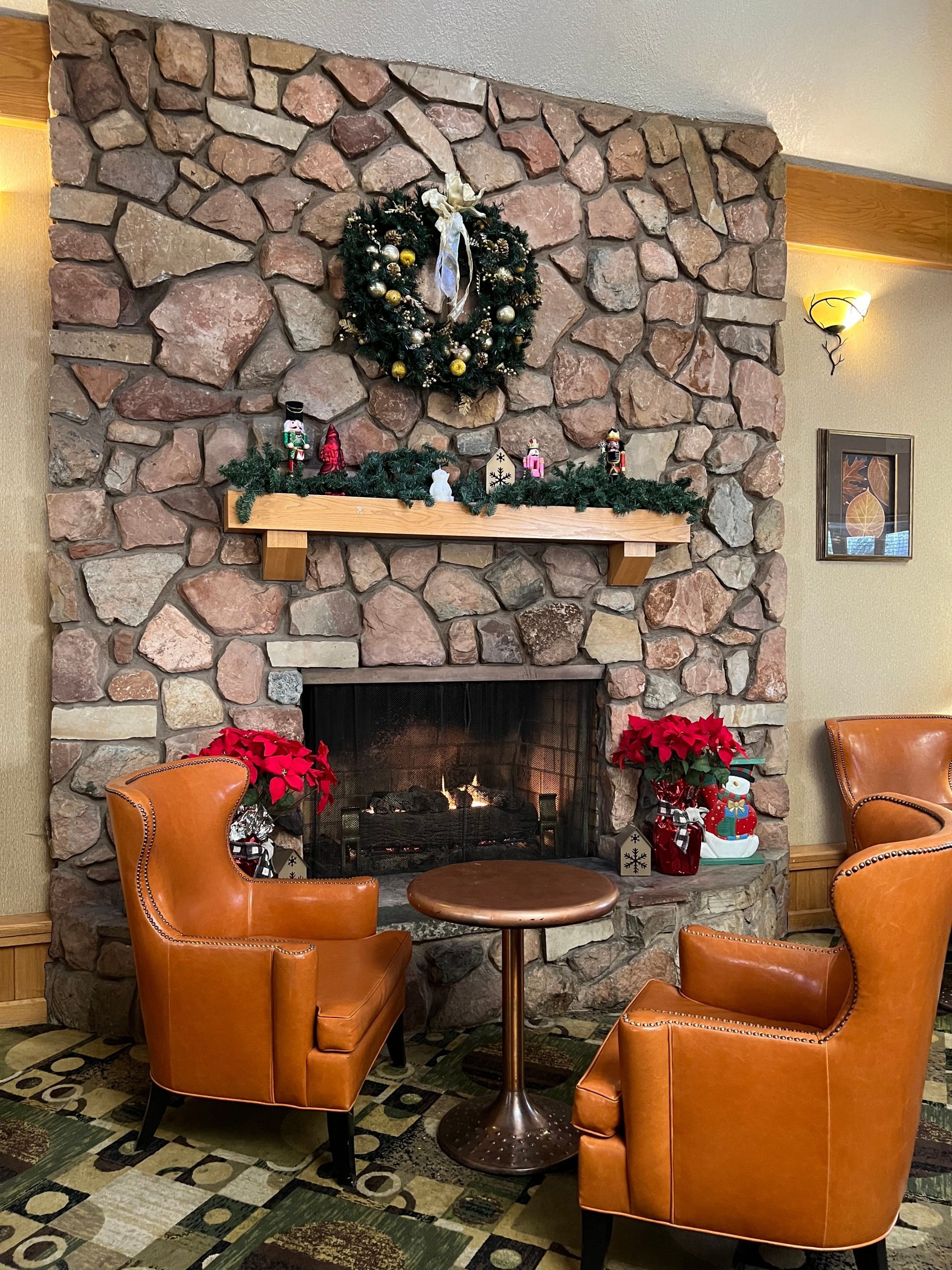 Warm living room setting with stone fireplace, armchairs, and festive holiday decor.