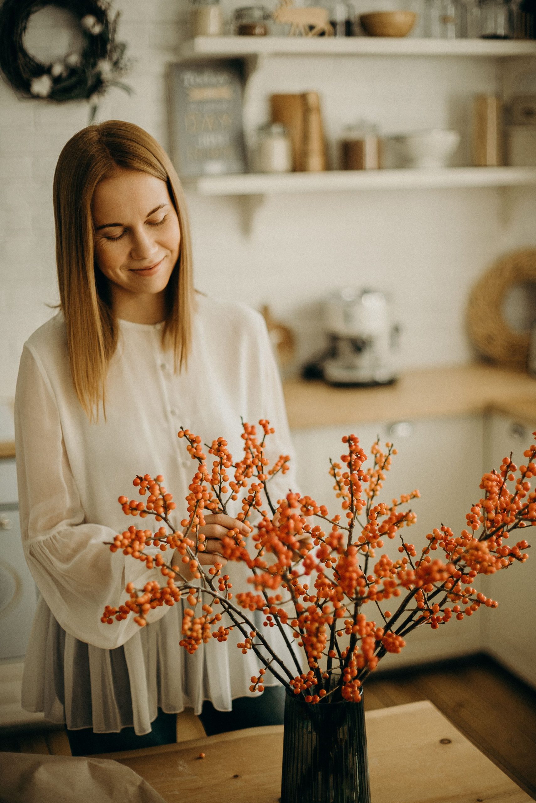 Woman arranging vibrant orange floral decoration in a cozy kitchen setting.