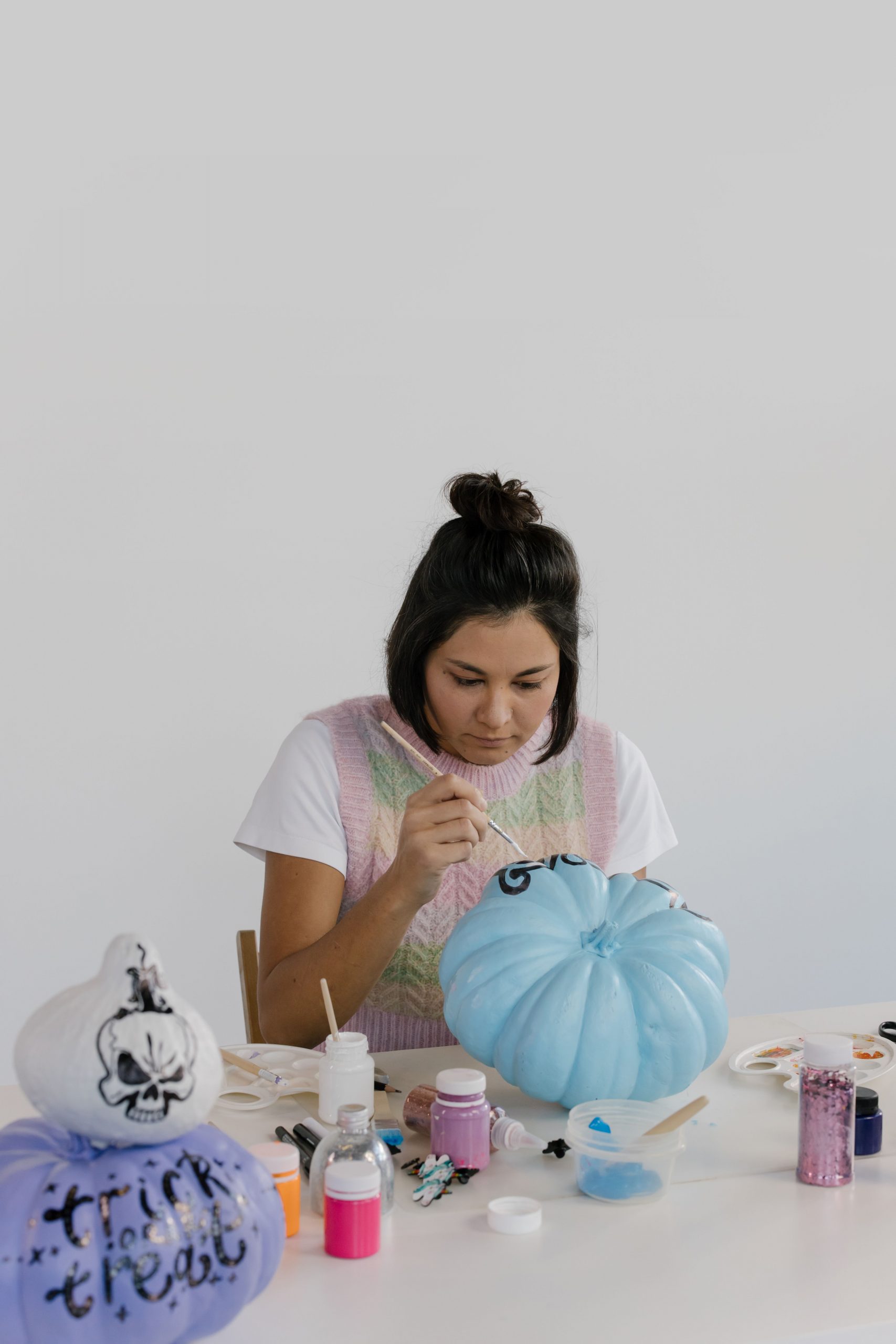 Woman painting colorful pumpkins with artistic designs for a festive Halloween decoration.