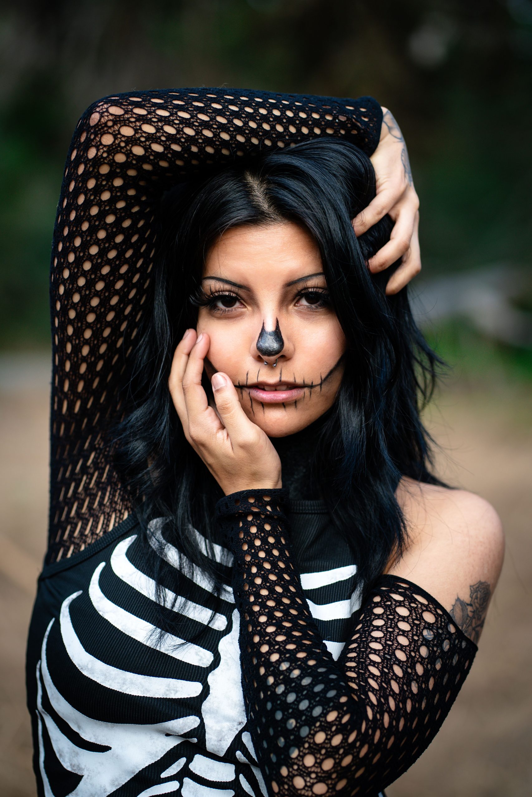 Woman with skeleton makeup poses outdoors embracing gothic style.