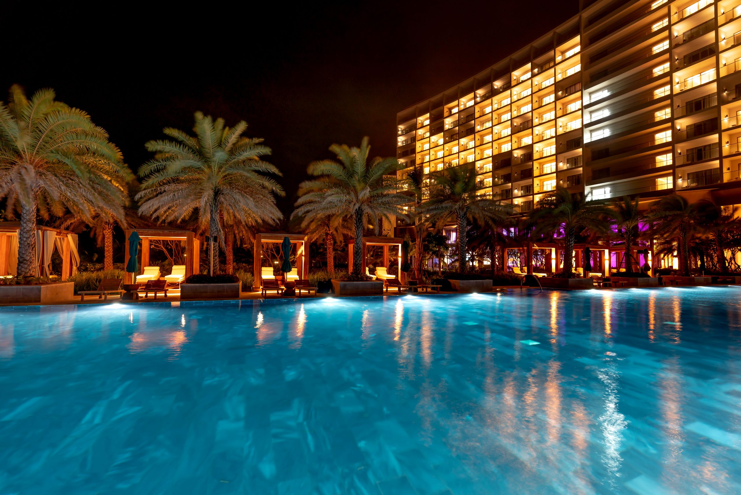 Stunning nighttime view of a hotel resort with beautifully lit swimming pool and palm trees.