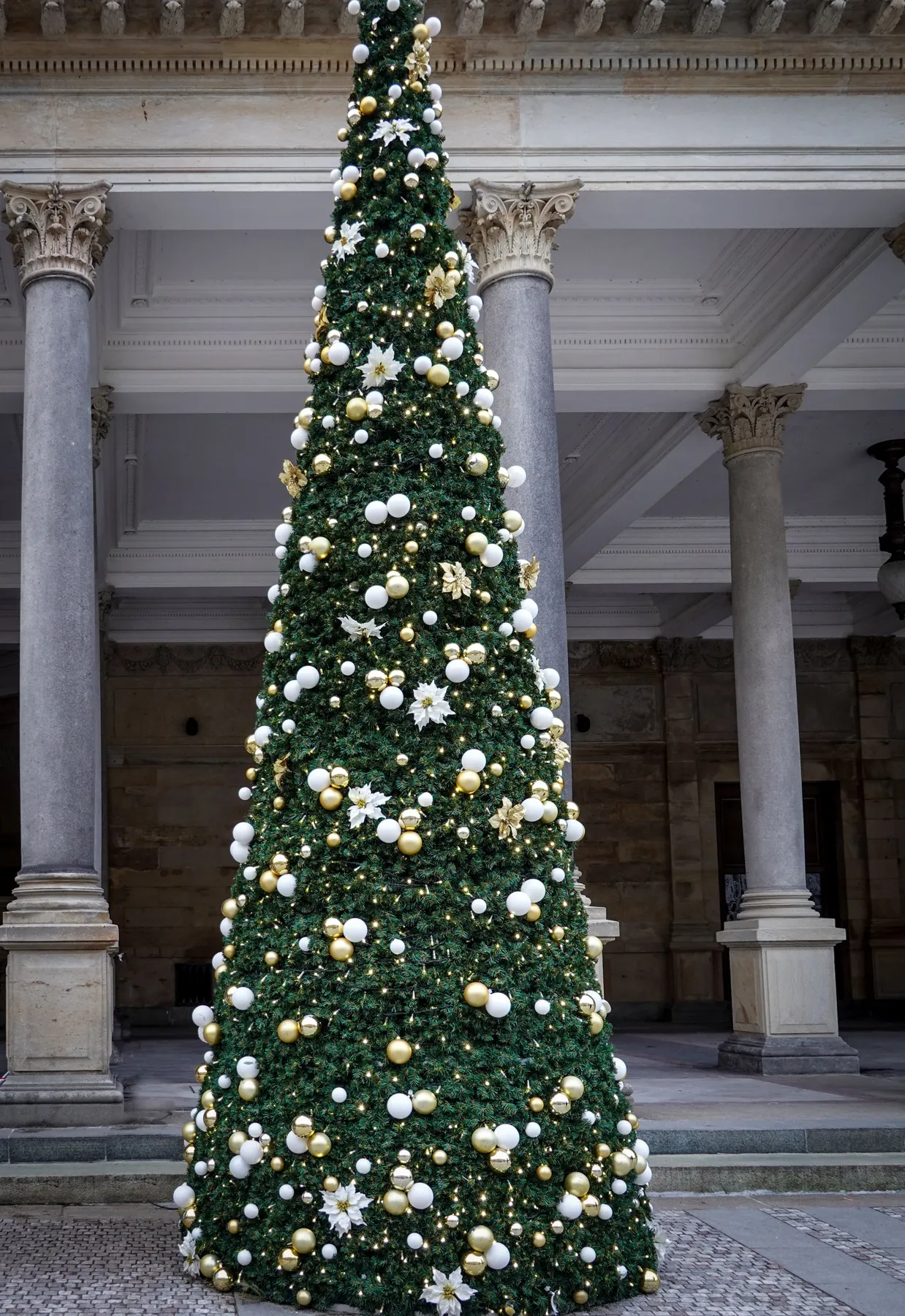 A beautifully adorned Christmas tree with gold and white decorations in an elegant town square.