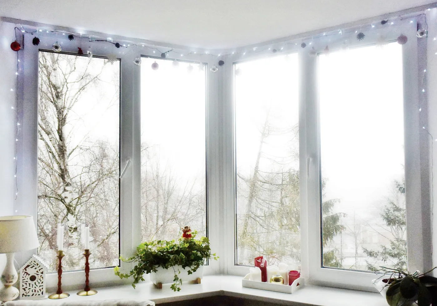 A bright winter window adorned with Christmas lights and decorations, creating a cozy festive atmosphere.