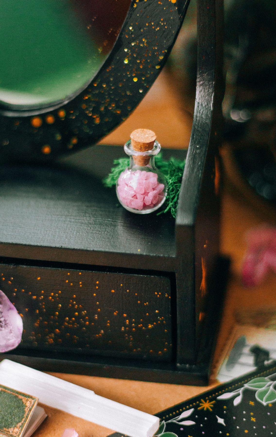 A close-up of a small corked vial with pink crystals on a decorative wooden box.