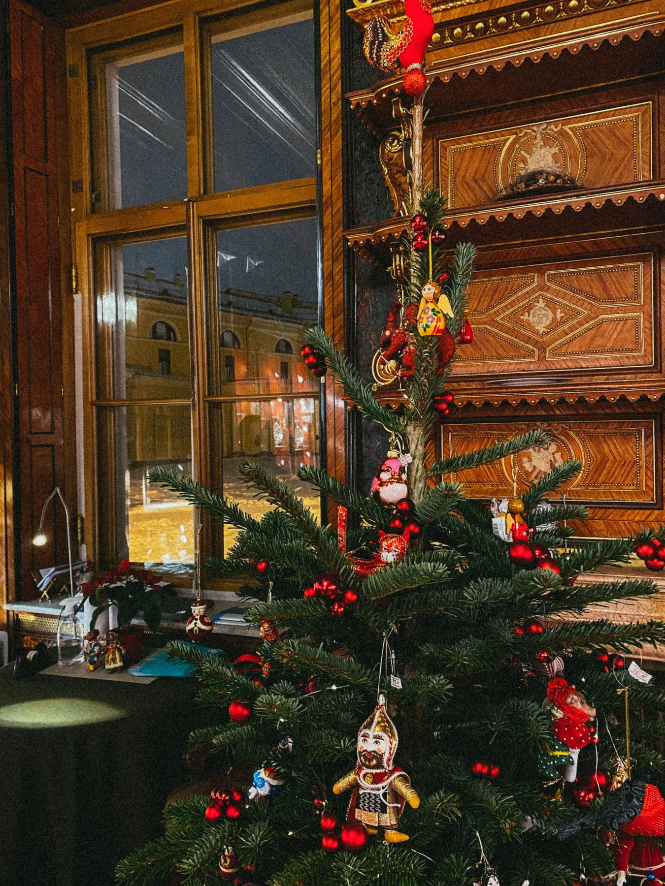 A cozy room with a decorated Christmas tree near a window at night.