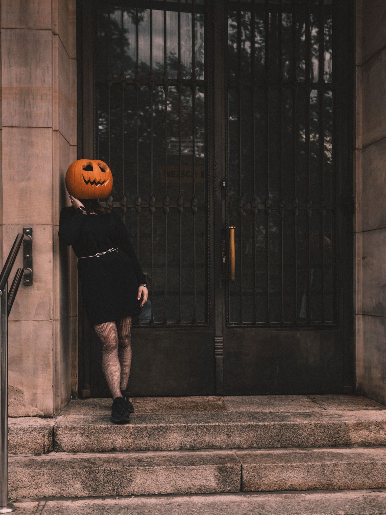 A figure with a pumpkin head leans against a gothic entrance, setting a spooky Halloween vibe.