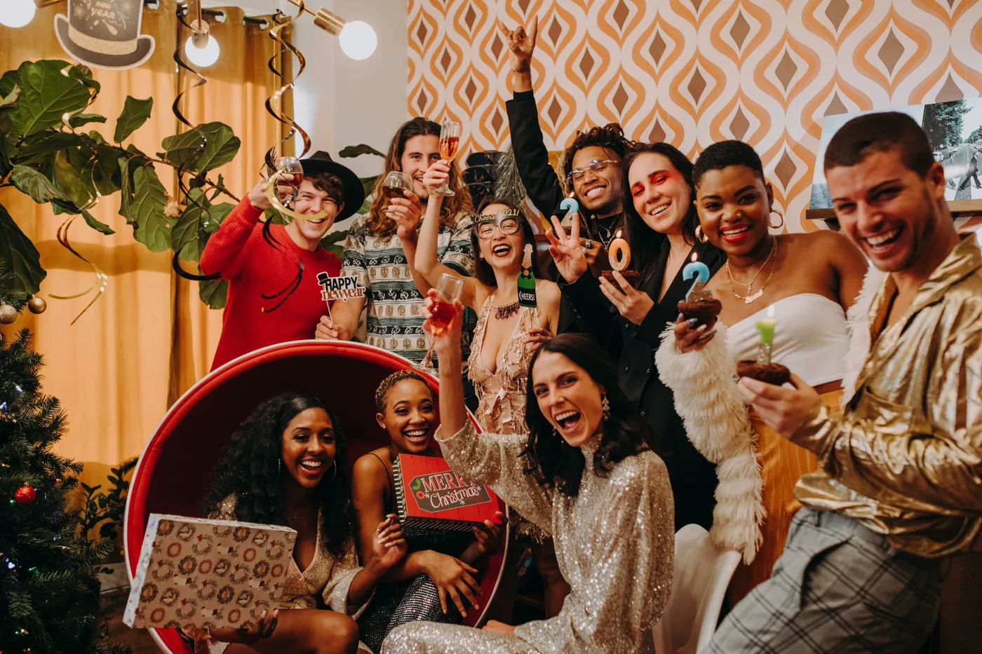 A lively party scene with a diverse group celebrating New Year's Eve indoors with drinks and decorations.