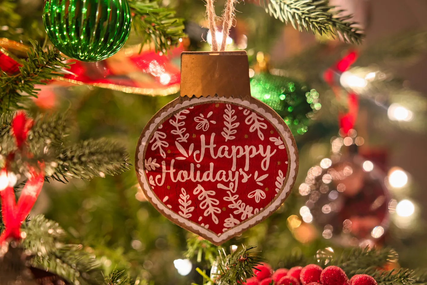A macro shot of a 'Happy Holidays' Christmas tree ornament