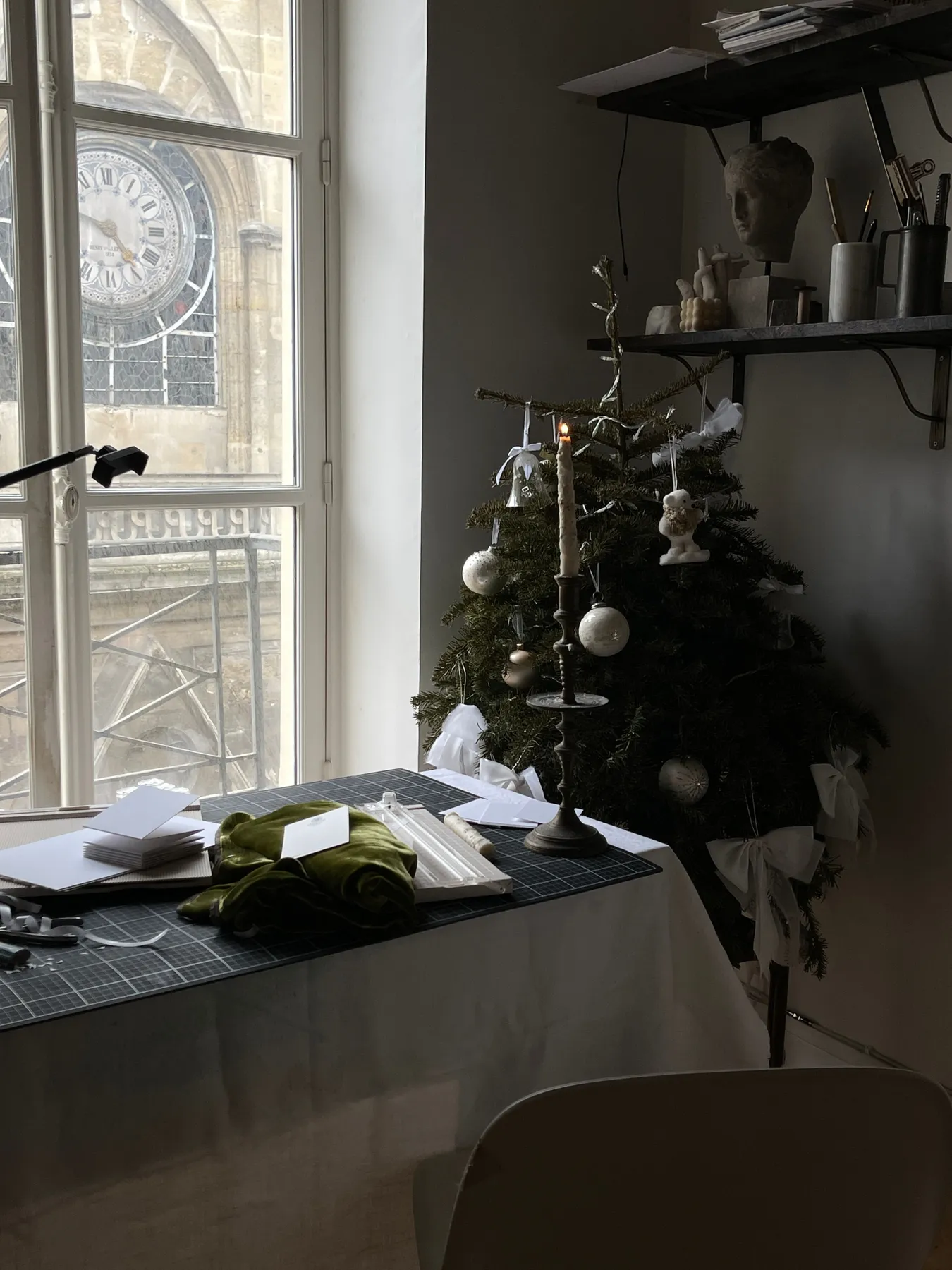 A peaceful indoor setup with a Christmas tree, candles, and papers on a desk.