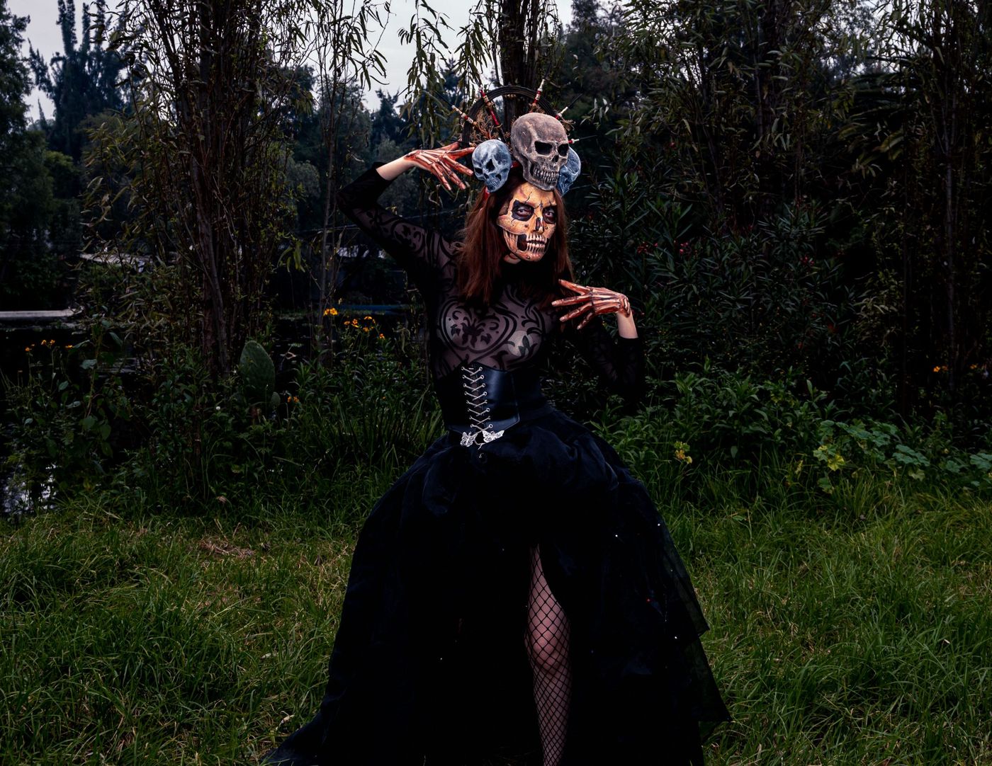 A person in gothic costume and skeleton makeup in a dark outdoor setting, evoking Halloween vibes.