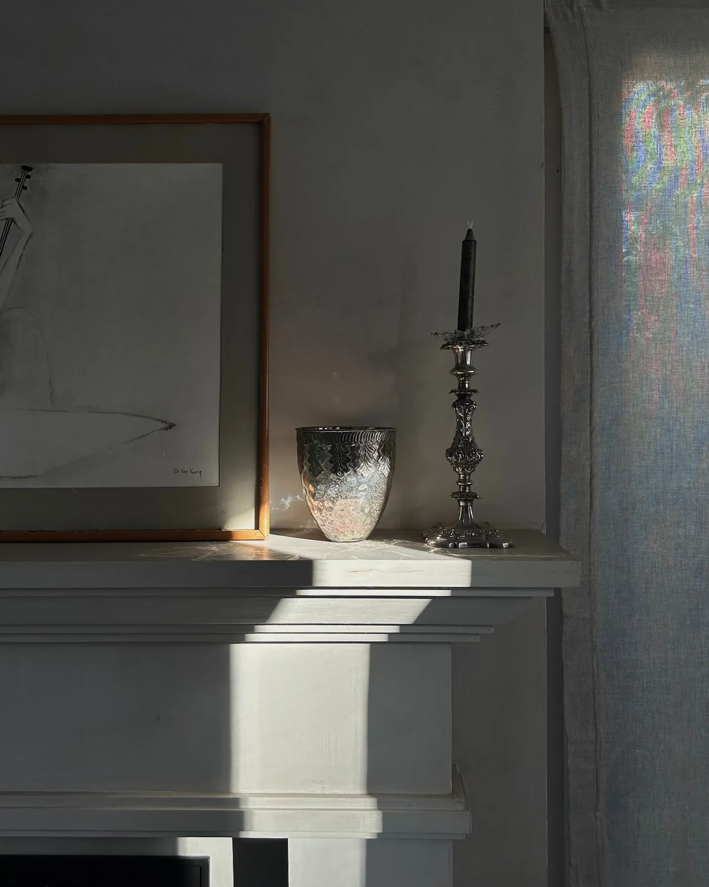 A serene still life of a fireplace mantel with a candle holder and framed art.