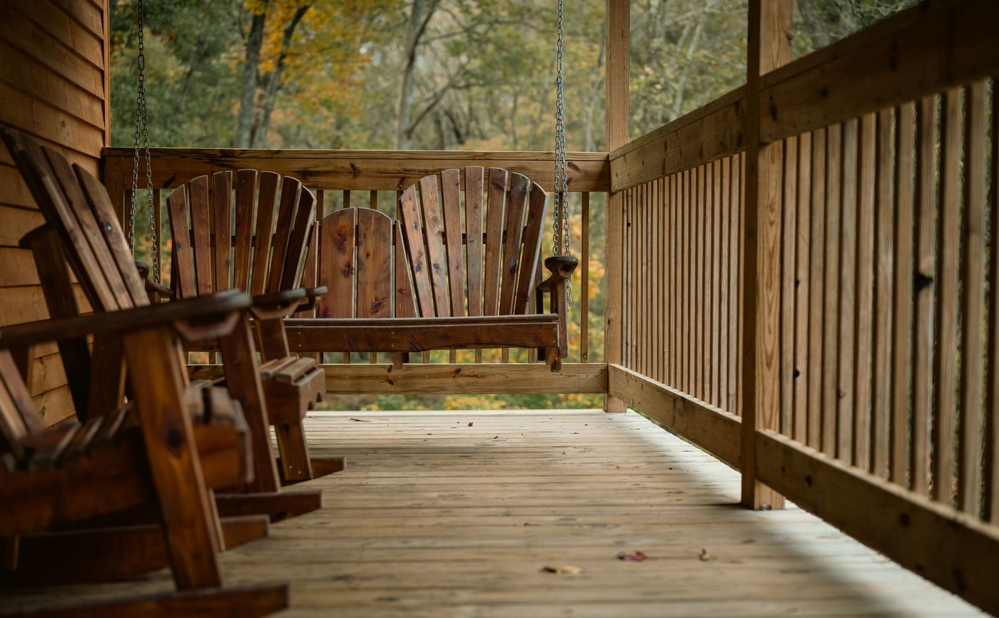 A serene wooden porch featuring a rustic hanging swing amidst autumnal foliage.