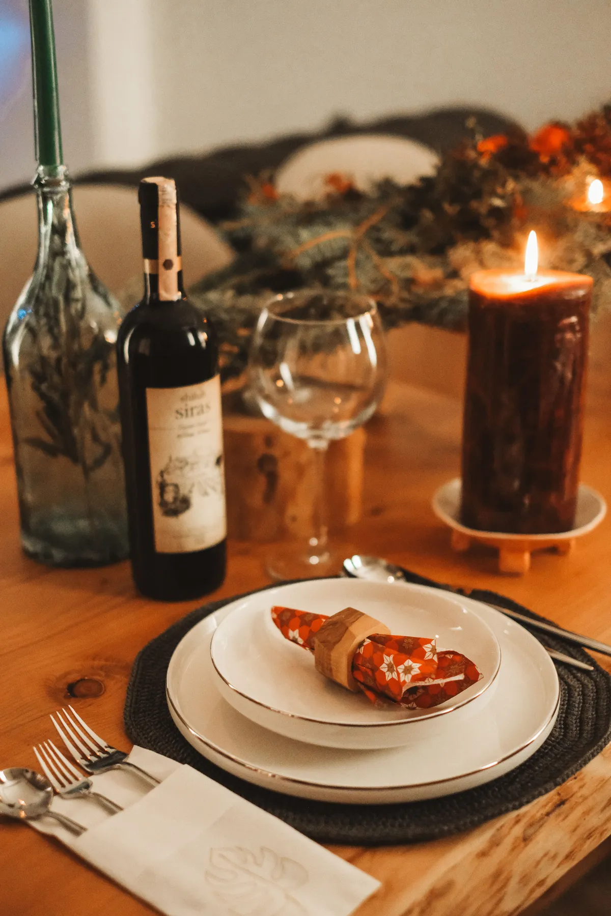 A sophisticated indoor table setup featuring wine, candlelight, and festive decor, perfect for holiday celebrations.