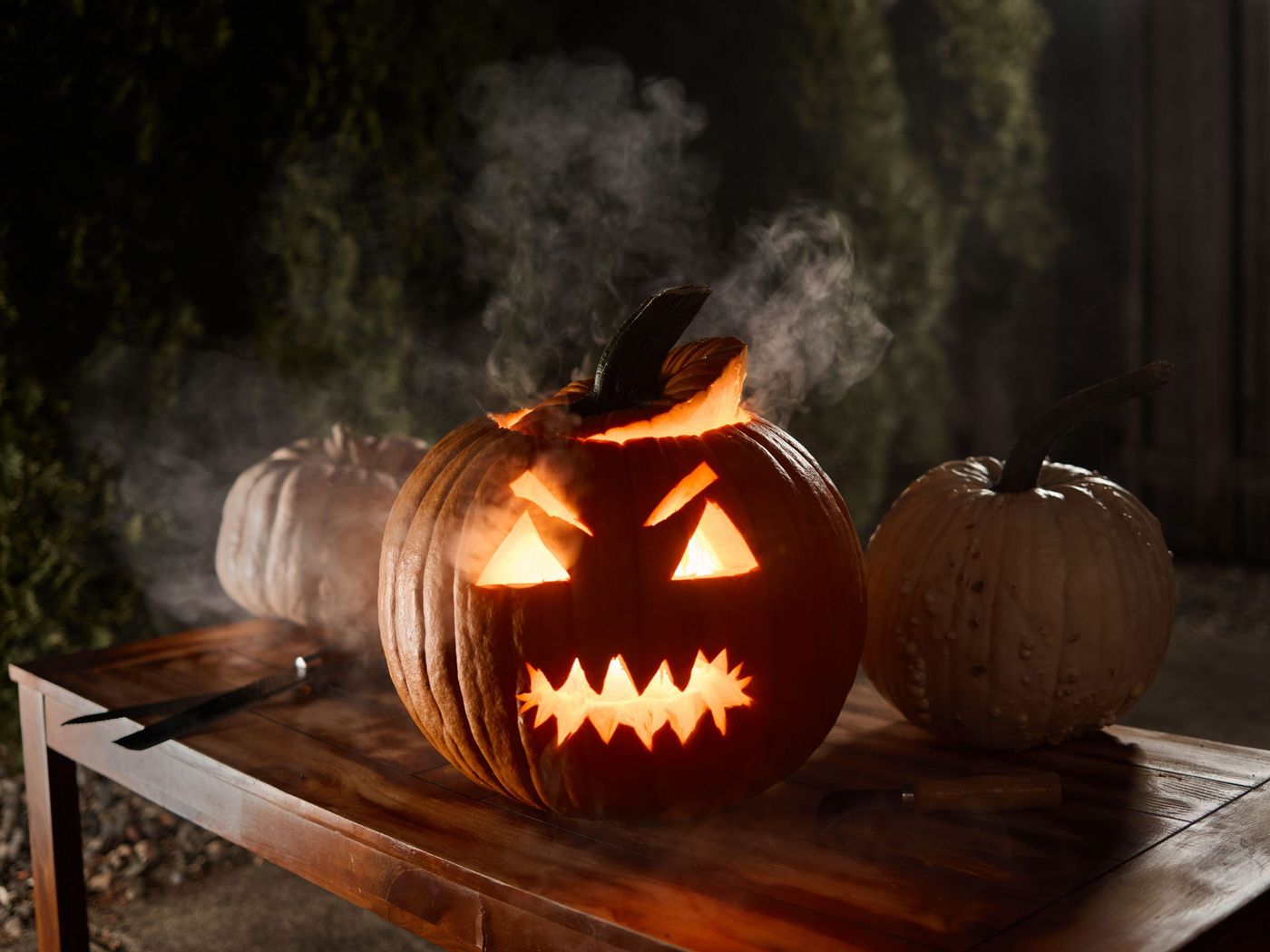 A spooky Jack-o'-lantern emits a warm glow illuminating a wooden table during Halloween night.