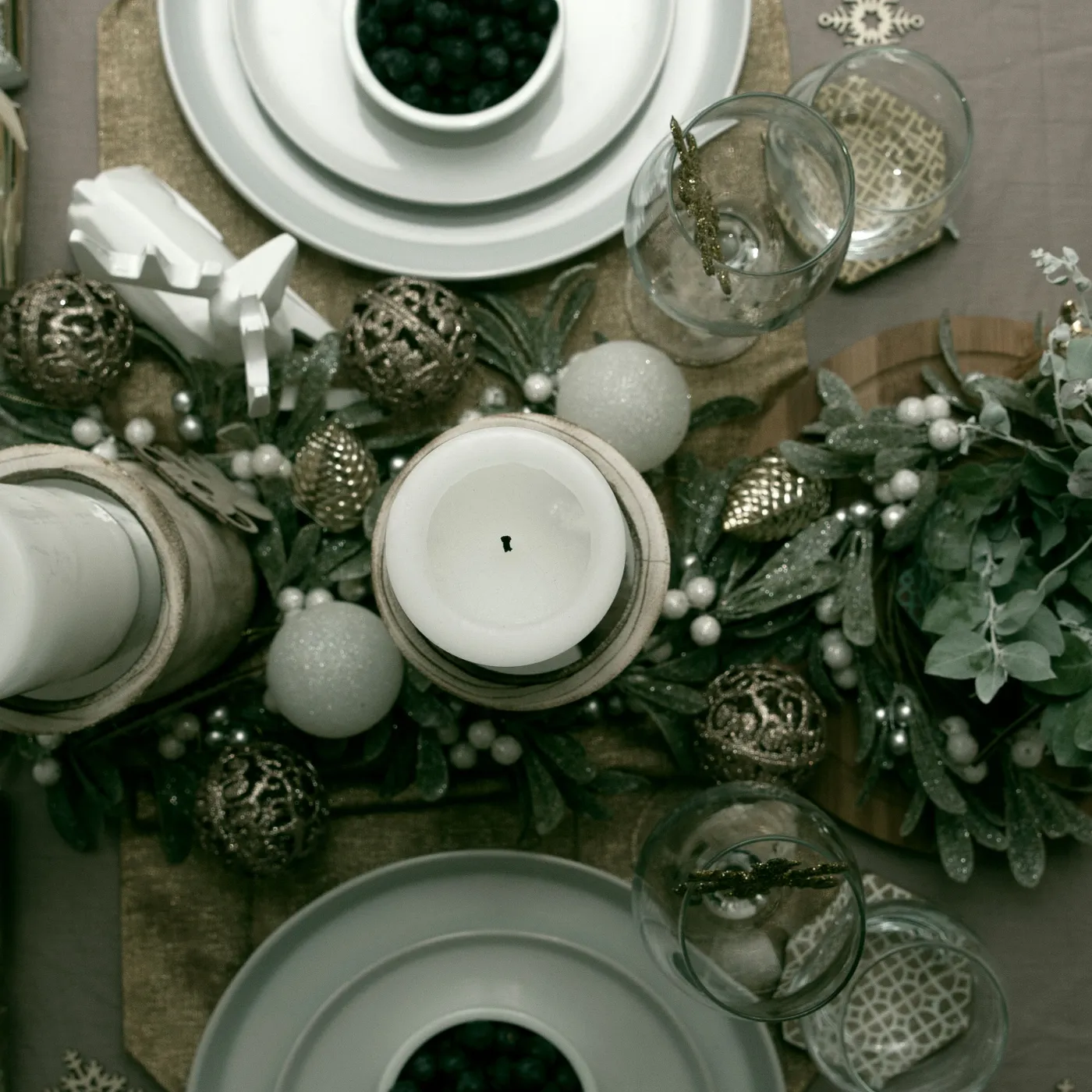 A top view of an elegant Christmas table setting featuring a candle centerpiece, ornaments, and dishware.