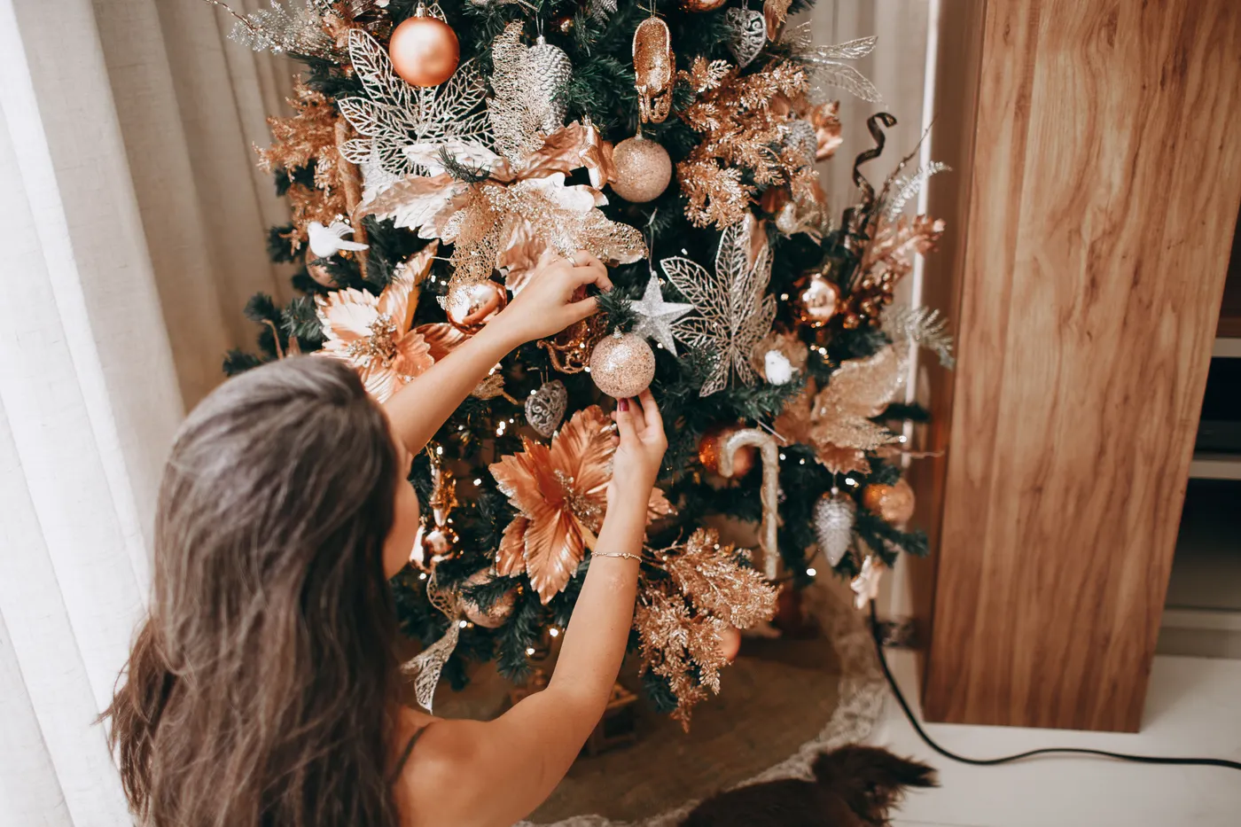 A woman decorates a beautifully adorned Christmas tree with golden ornaments, creating a festive holiday atmosphere.