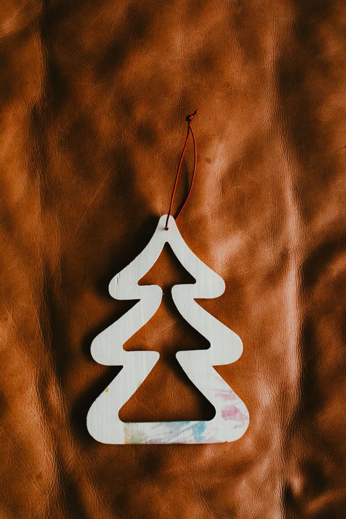 A wooden Christmas tree ornament with a simple design on a leather background.