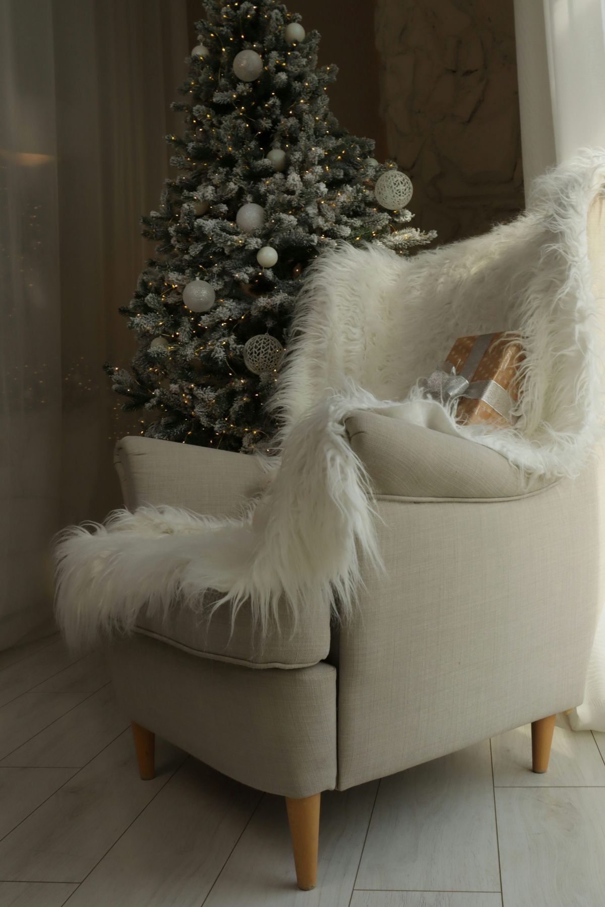 Armchair with fluffy blanket and gift near christmas tree