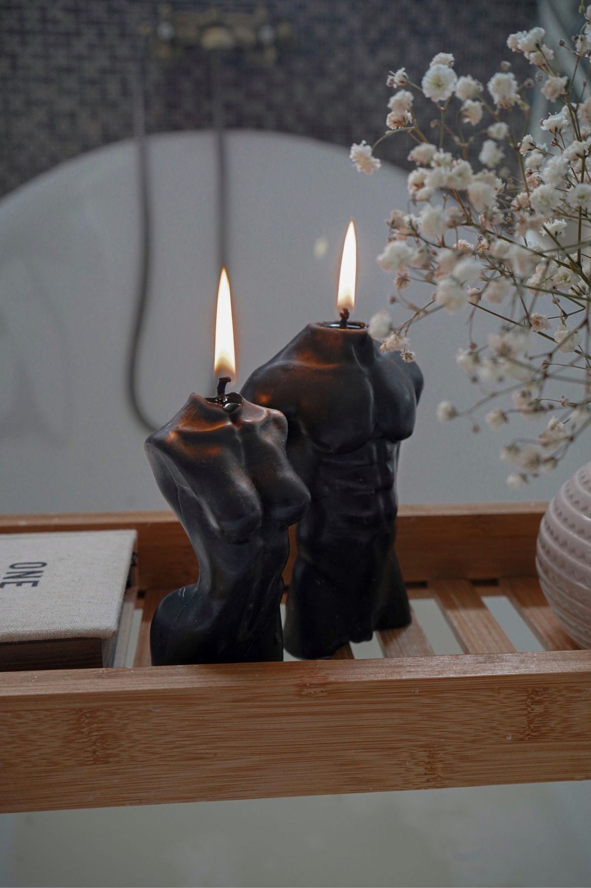 Artistic candles shaped like human torsos, accompanied by delicate flowers, create a serene atmosphere.