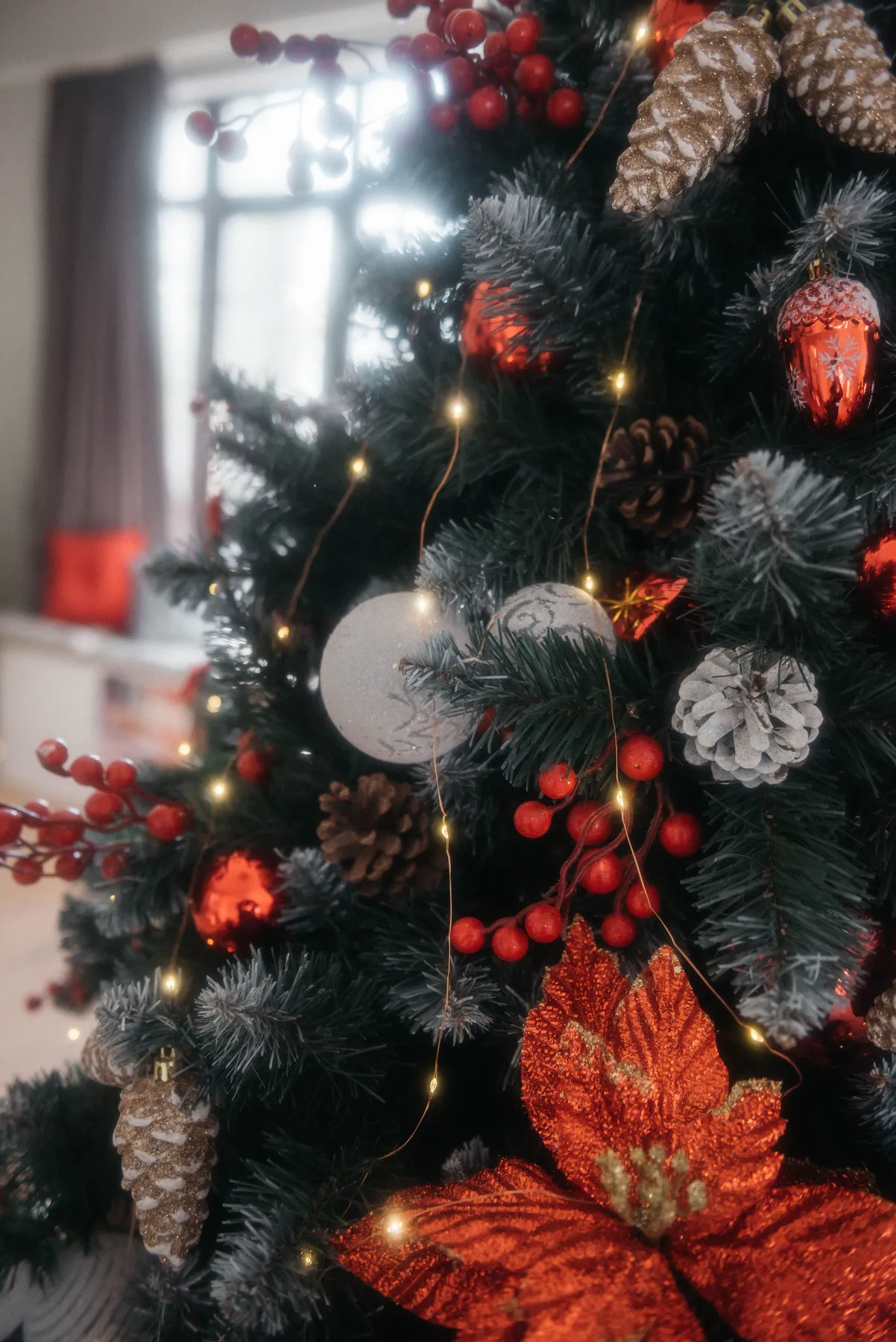 Beautiful Christmas tree adorned with red ornaments, berries, pinecones, and twinkling lights.