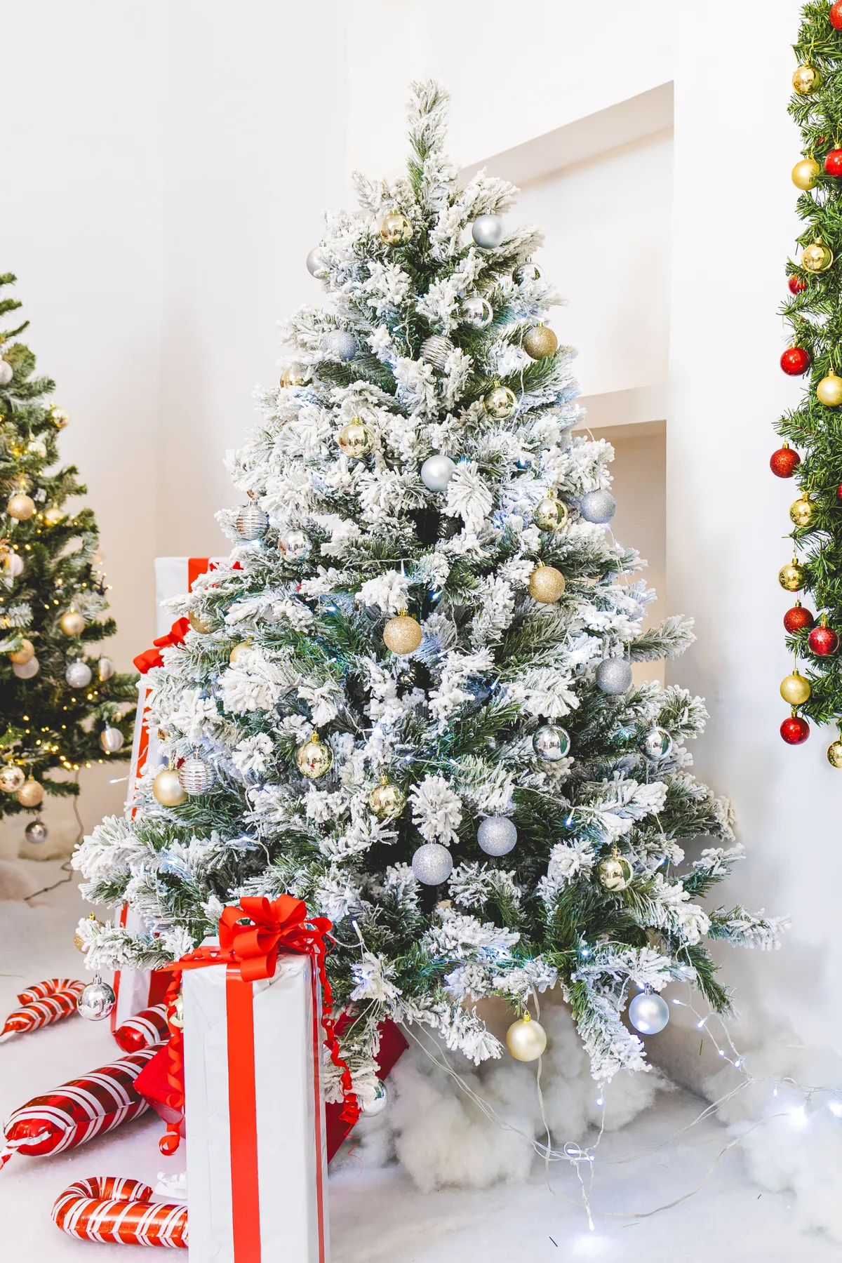 Beautifully decorated snowy Christmas tree with gifts and ornaments indoors.