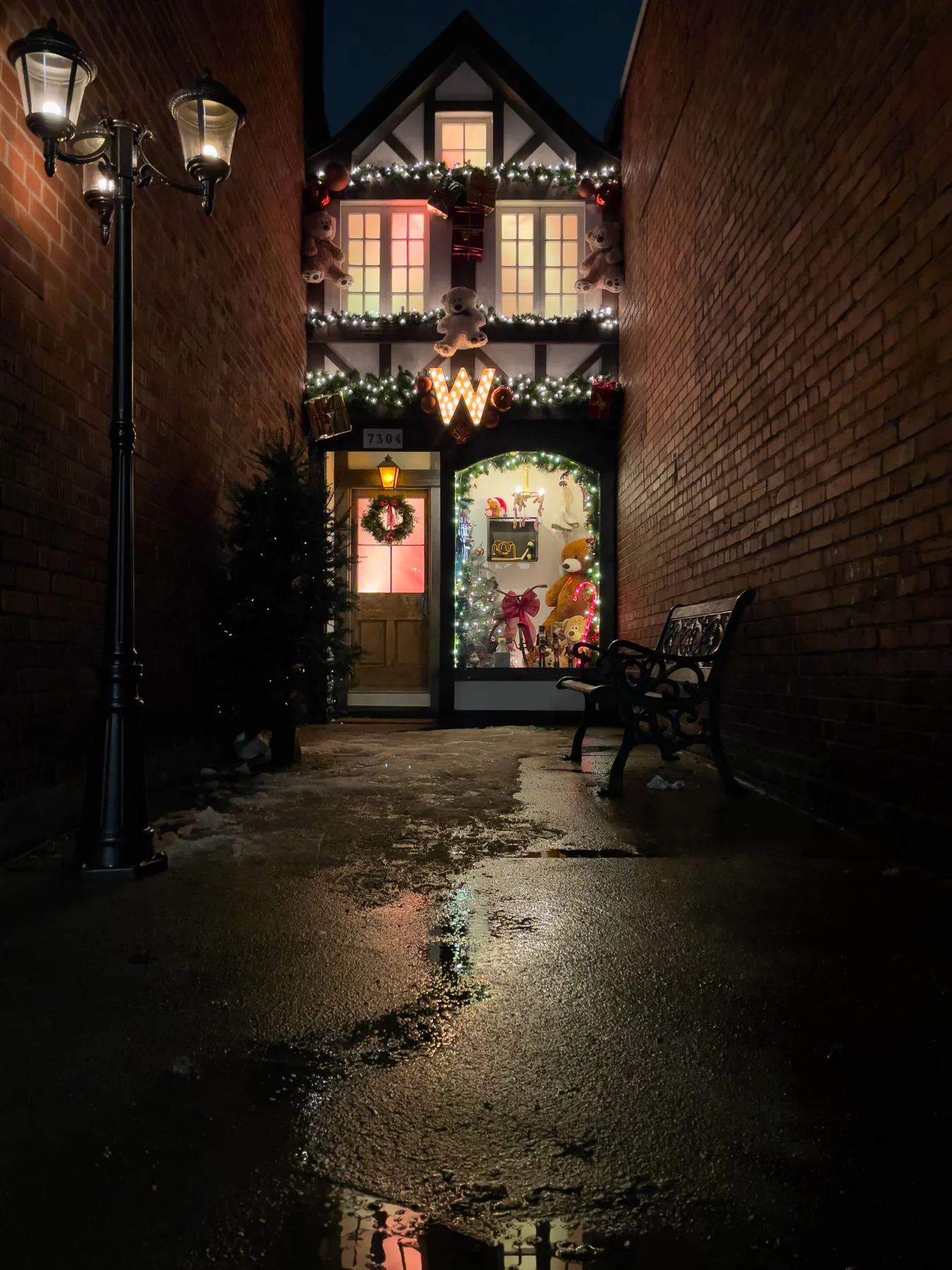 Charming alleyway with Christmas lights, decorations and a shop display at night.