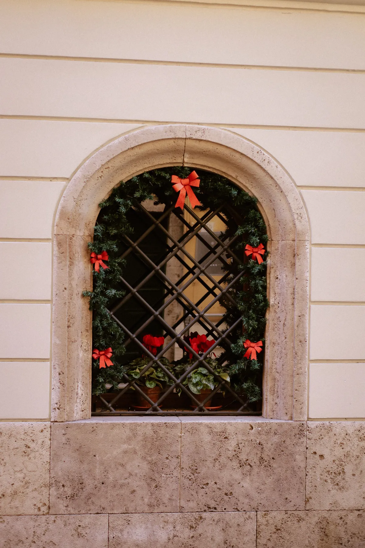 Charming arched window with festive Christmas wreath and red bows, framed in old stone.